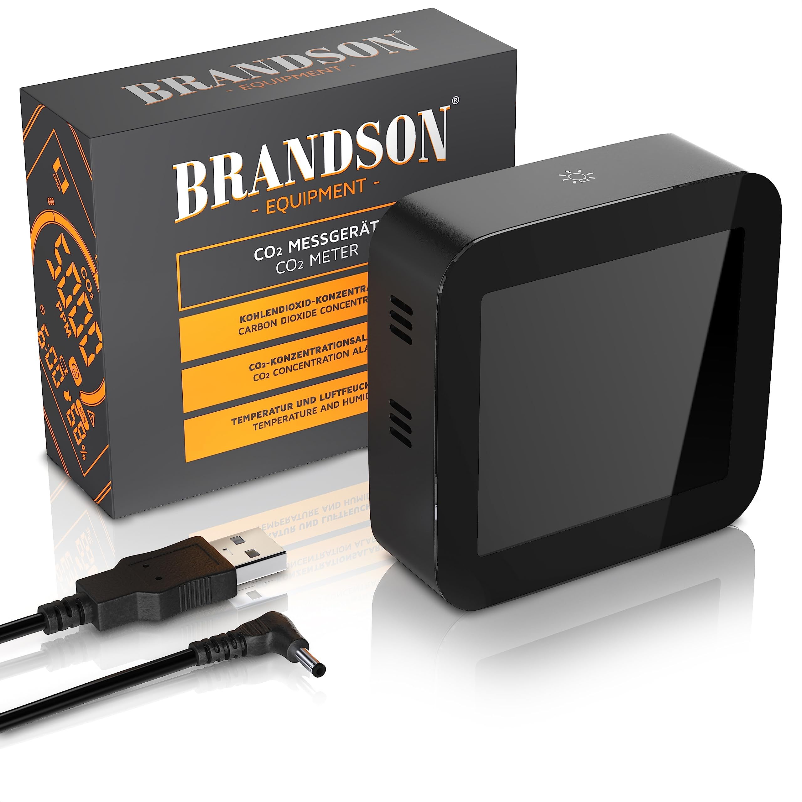 Un misuratore di CO2 nero con display, la sua scatola e un cavo USB su sfondo bianco.