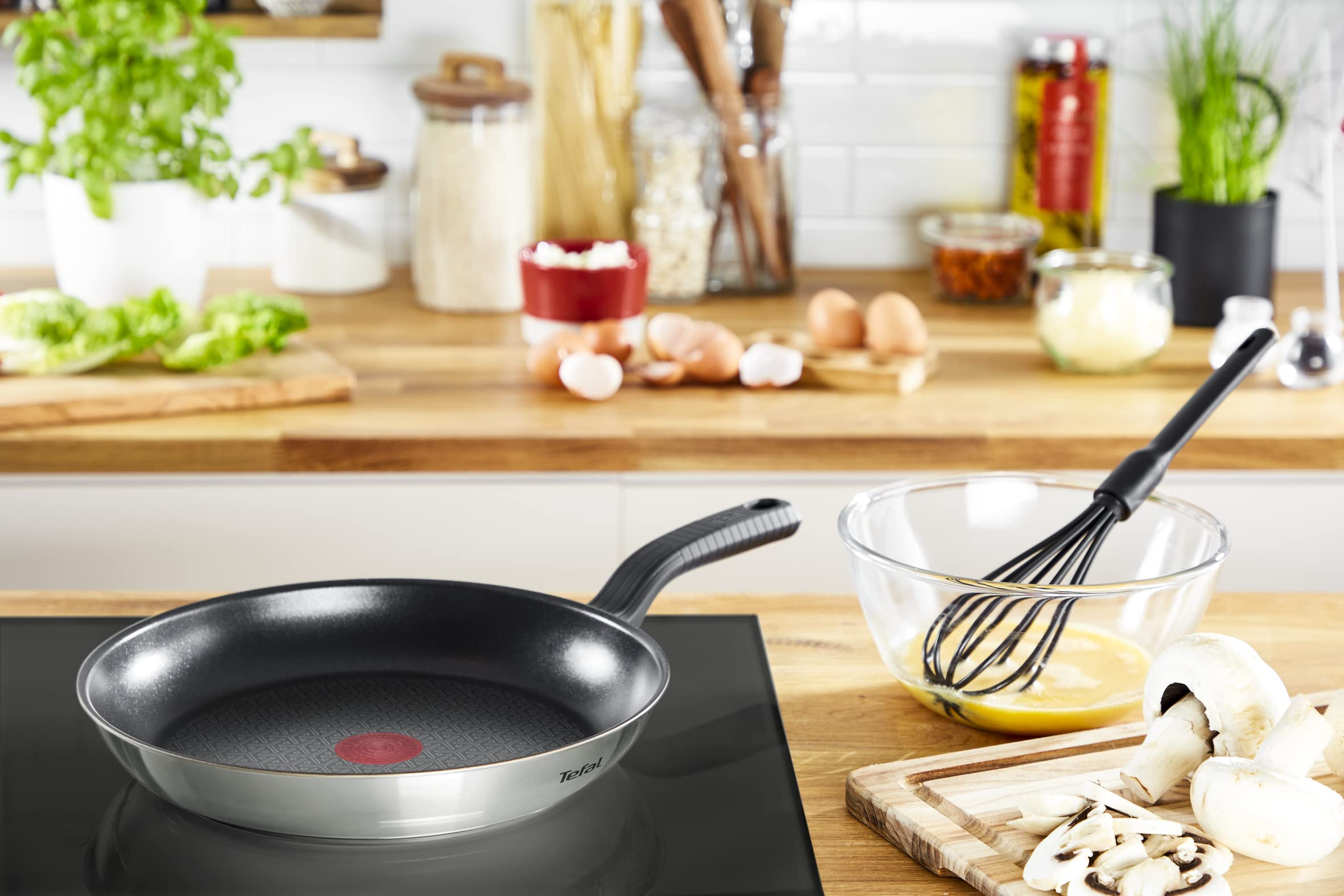 Une poêle Tefal sur la cuisinière, un bol d'œufs battus, des champignons sur une planche et un décor de cuisine.