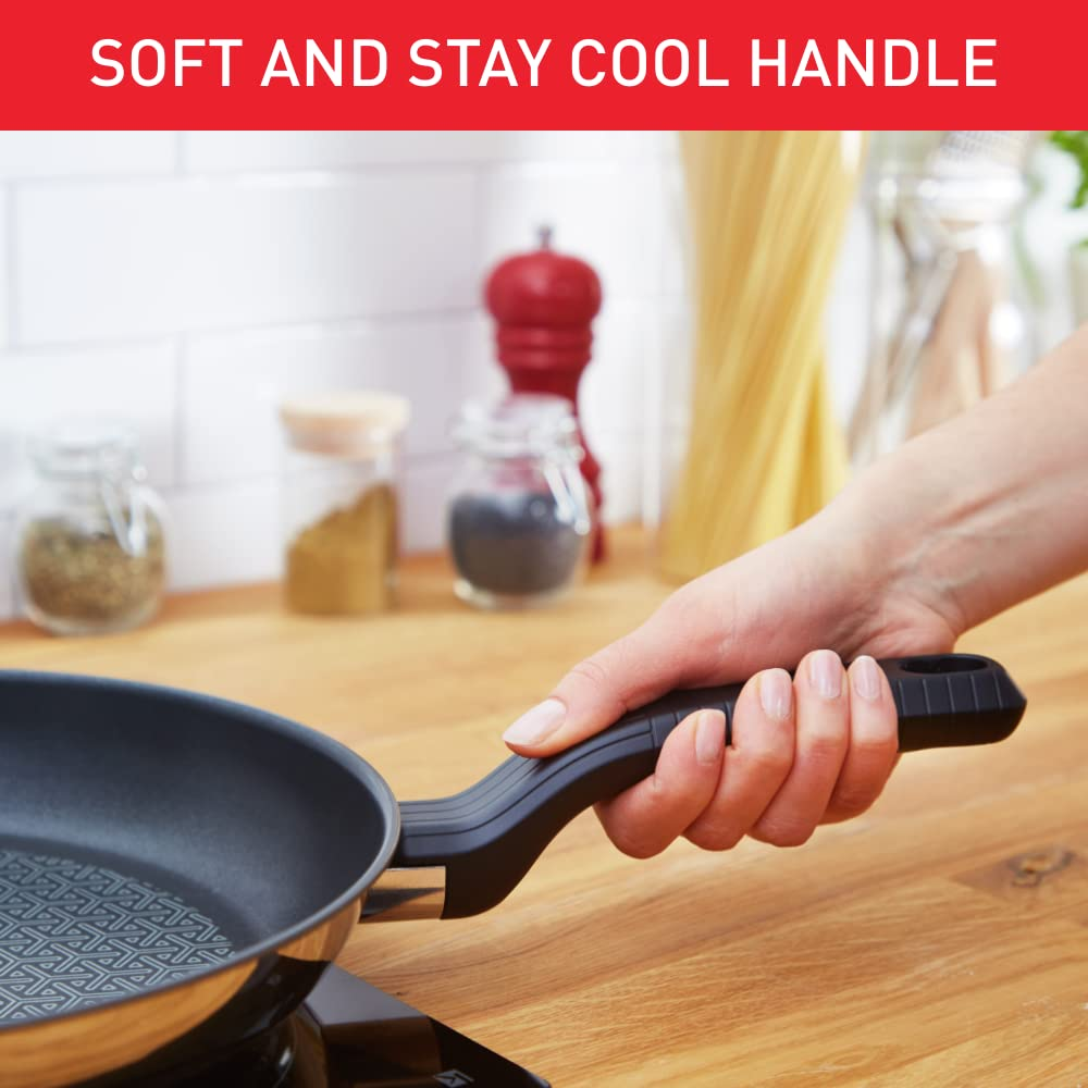 Une main tenant la poignée noire et ergonomique d'une poêle dans une cuisine lumineuse.