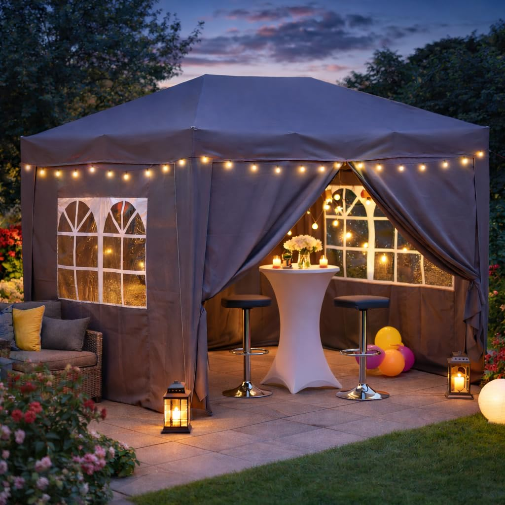 Une tente de fête grise dans un jardin au crépuscule, illuminée par des guirlandes et des lanternes.