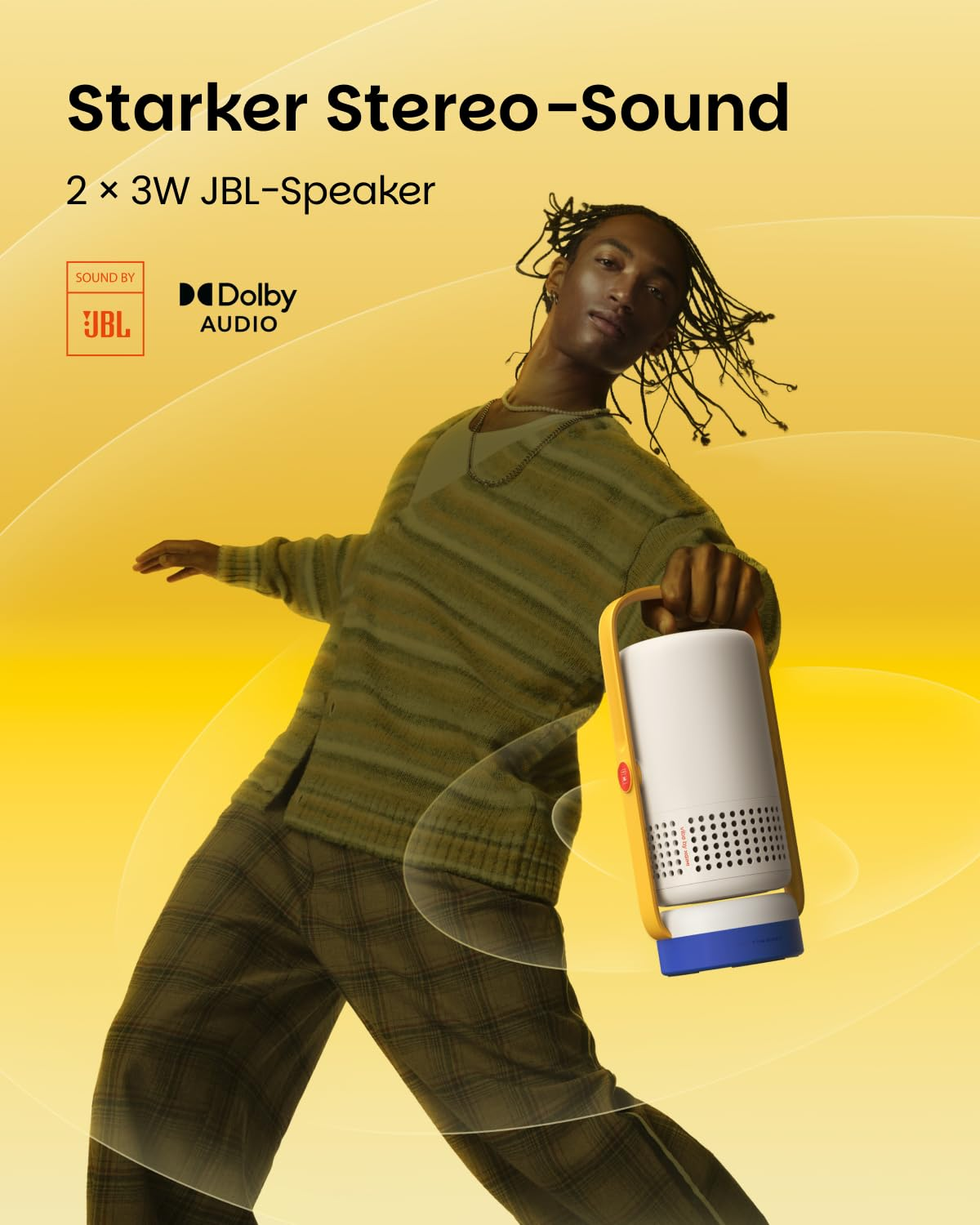 Un uomo con i dreadlocks tiene in mano un altoparlante portatile JBL su sfondo giallo.