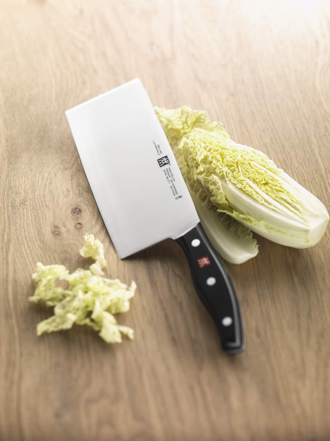 Ein großes Küchenmesser mit schwarzem Griff und chinesischer Klinge liegt neben Nackenkohl auf einer Holzunterlage.