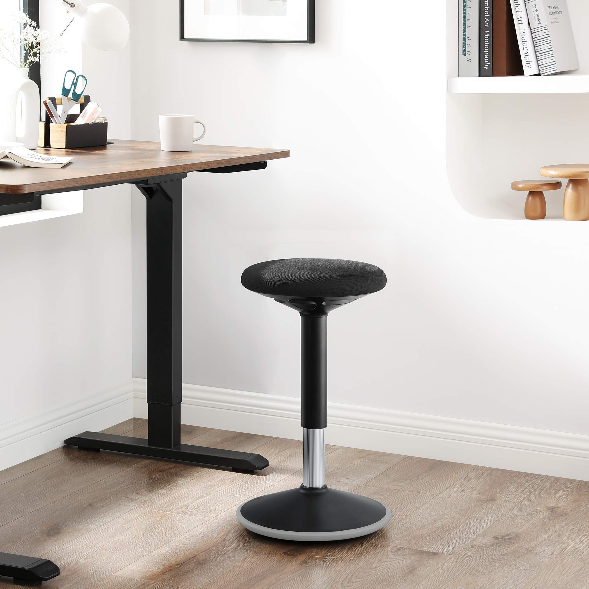 Un tabouret ergonomique noir réglable se trouve dans un bureau moderne avec parquet et bureau.