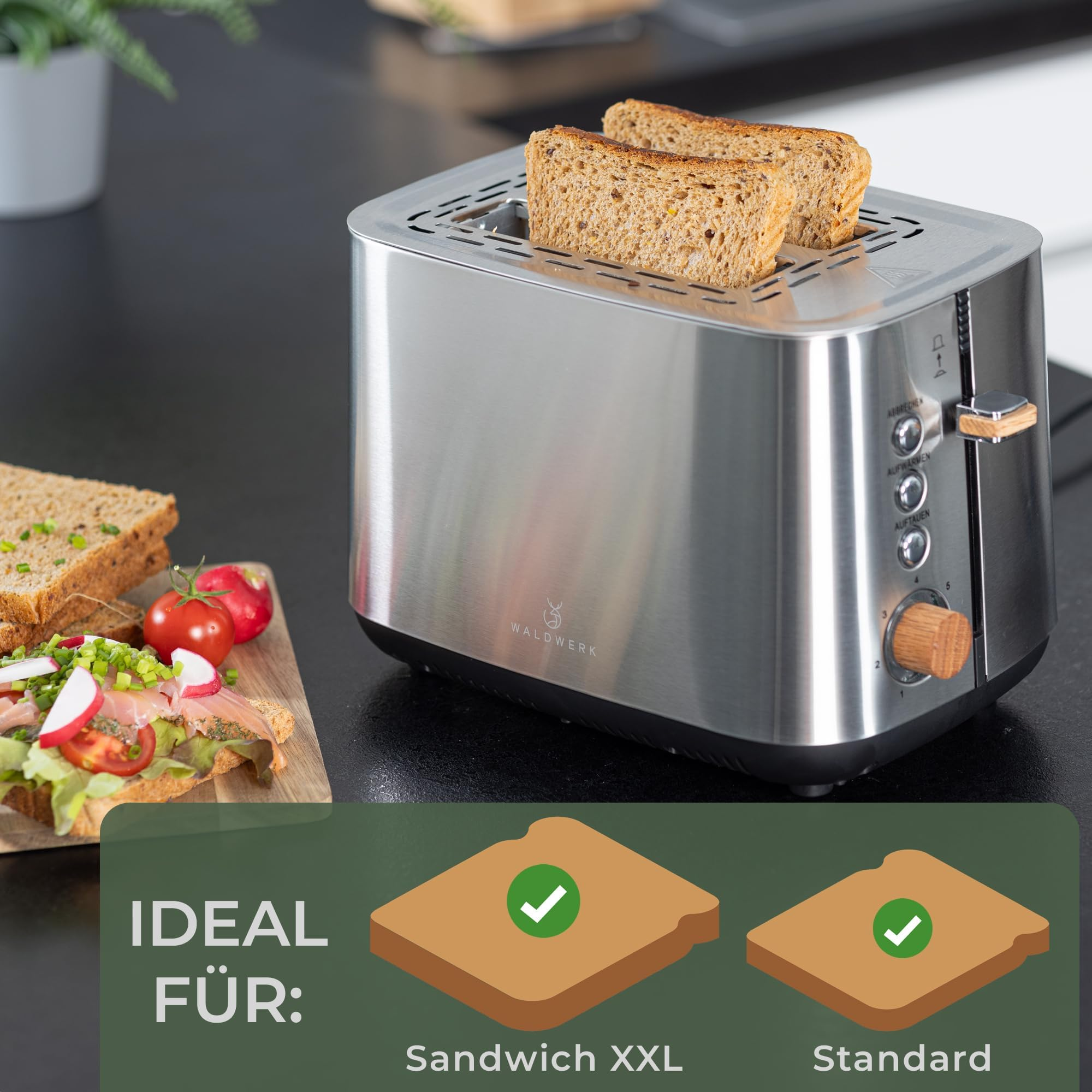 Un tostapane in acciaio inossidabile con due fette di pane su un piano cucina, vicino a un panino e pomodori.