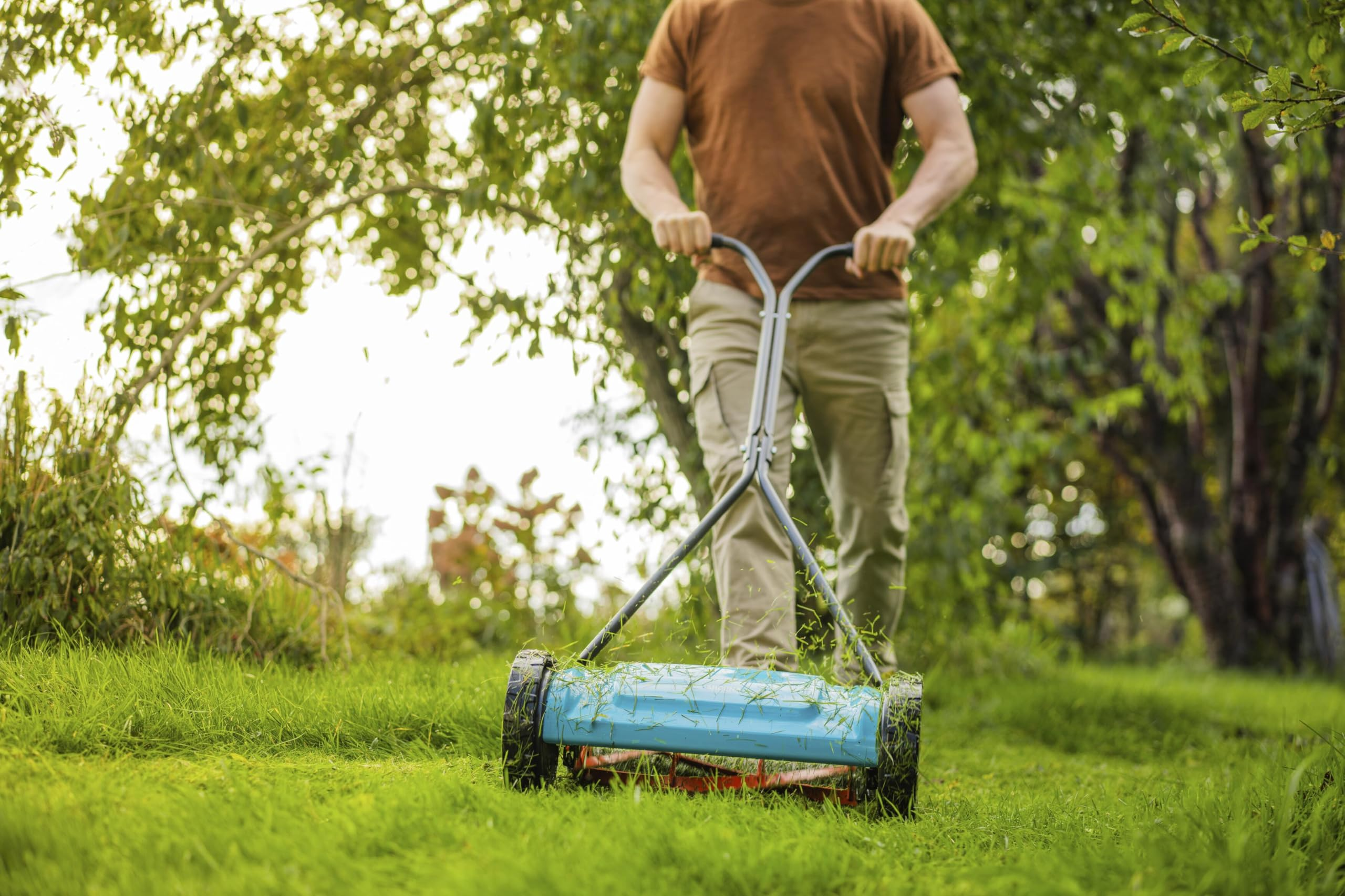 Un homme tond l'herbe verte d'un jardin avec une tondeuse à gazon manuelle par une journée ensoleillée.