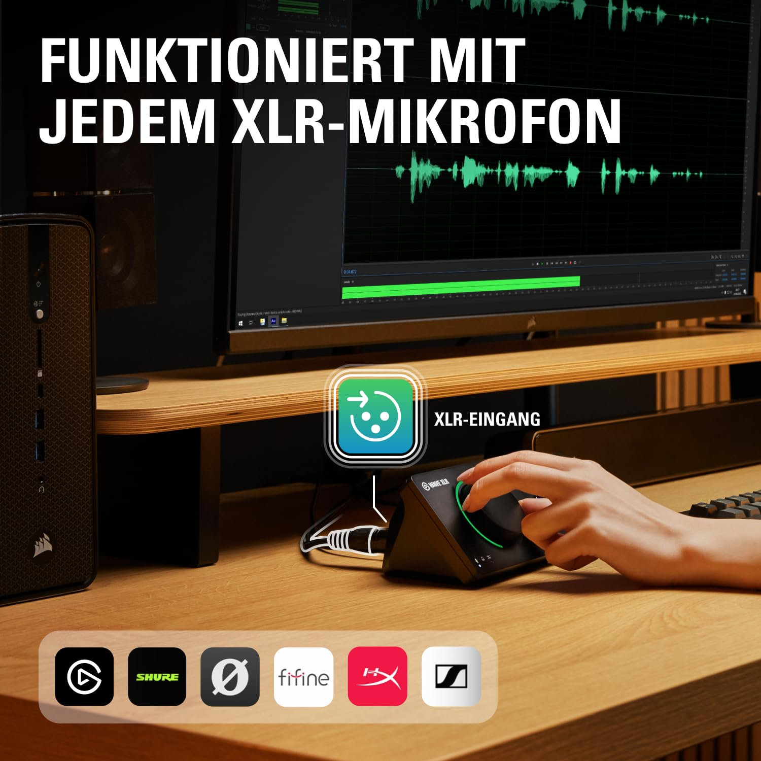 Hand bedient ein schwarzes Audiogerät auf einem Schreibtisch mit Monitor im Hintergrund.