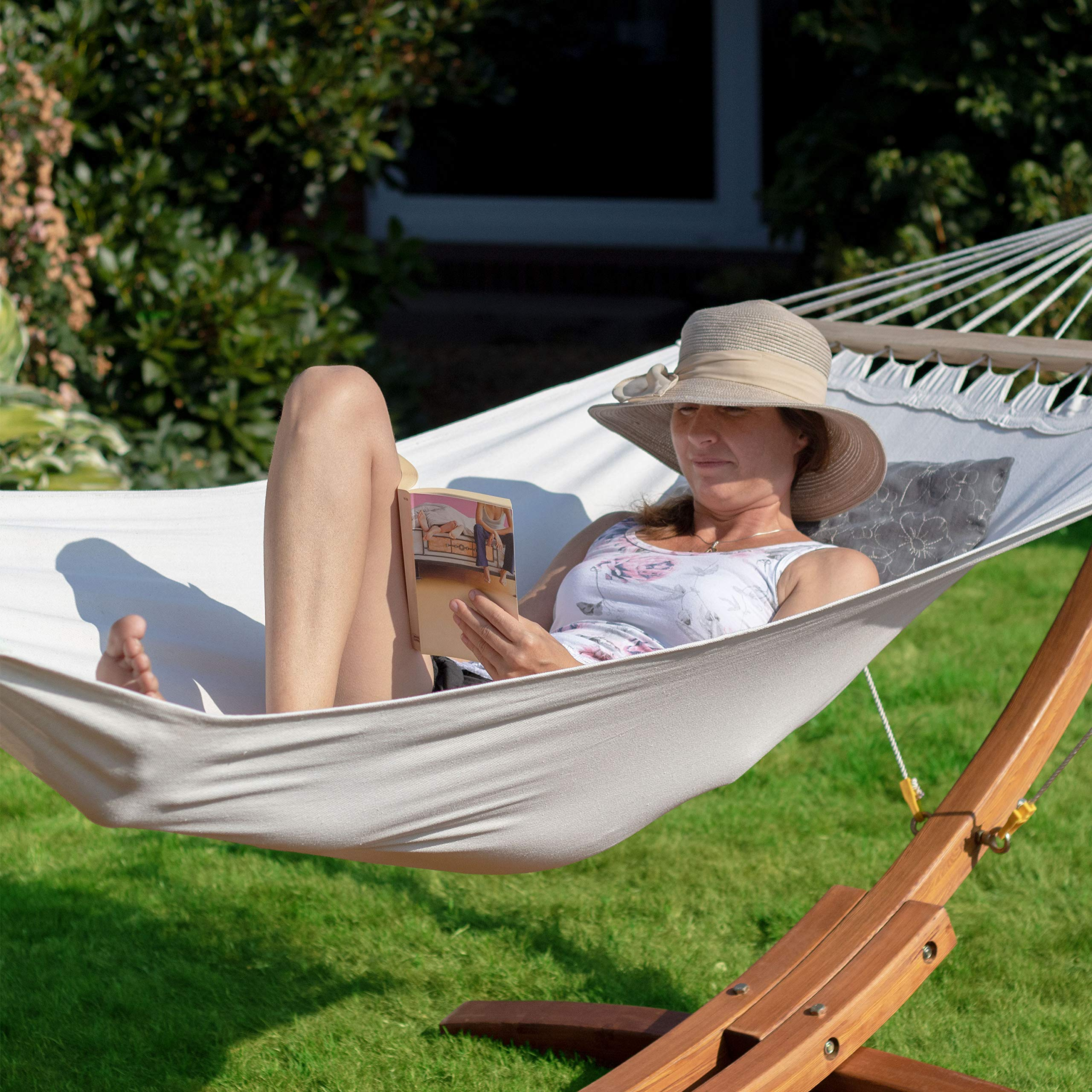 Eine Frau mit Hut liest ein Buch in einer weißen Hängematte im Garten.