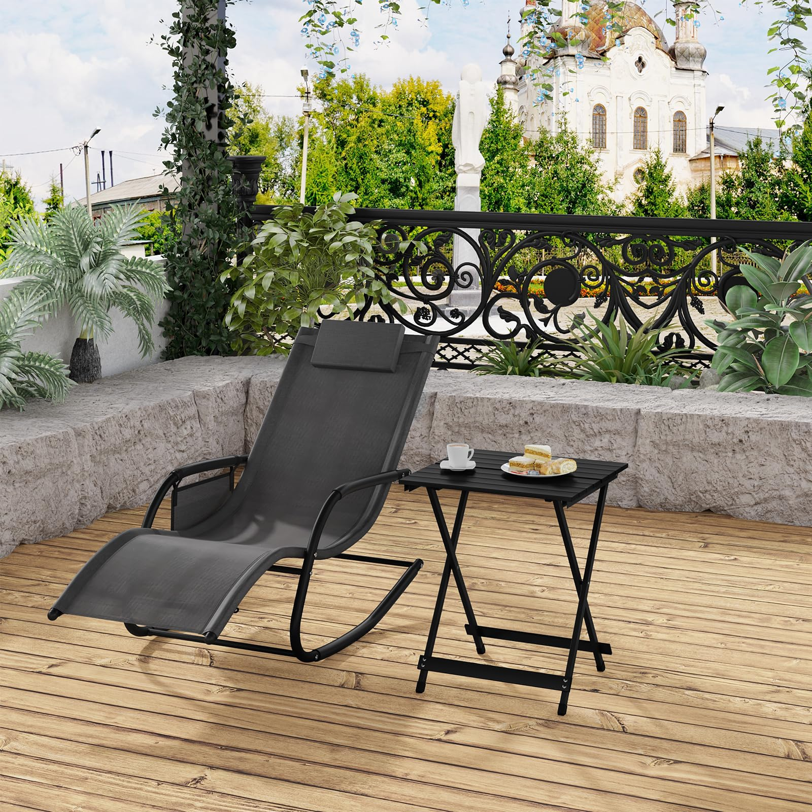 Una sedia a dondolo nera e un tavolino con caffè e torta su un patio in legno con sfondo panoramico.