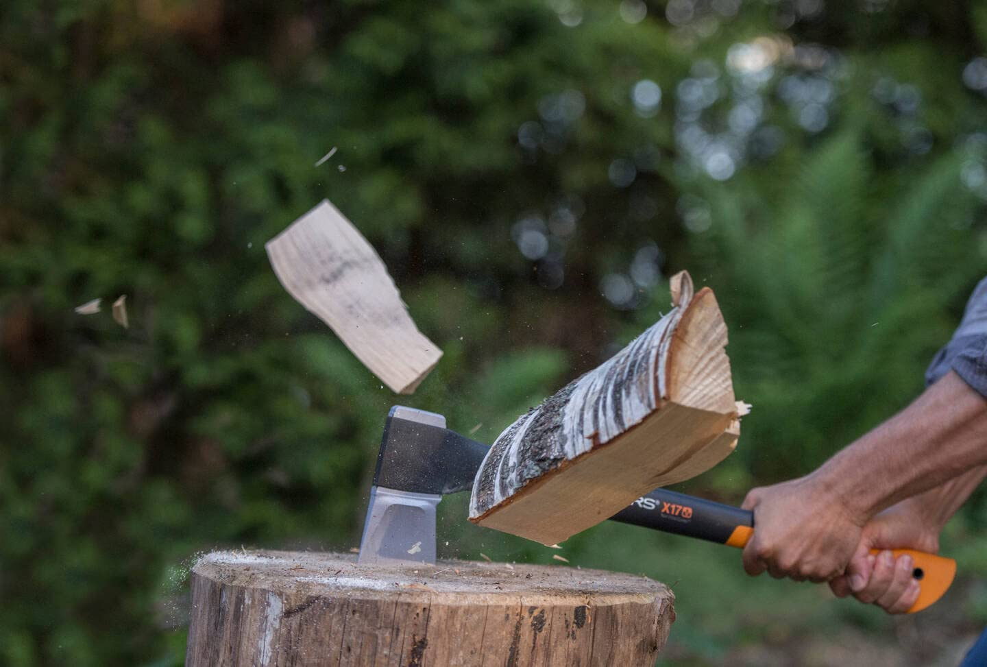 Eine Axt spaltet einen Holzscheit auf einem Baumstamm, während Holzteile durch die Luft fliegen.