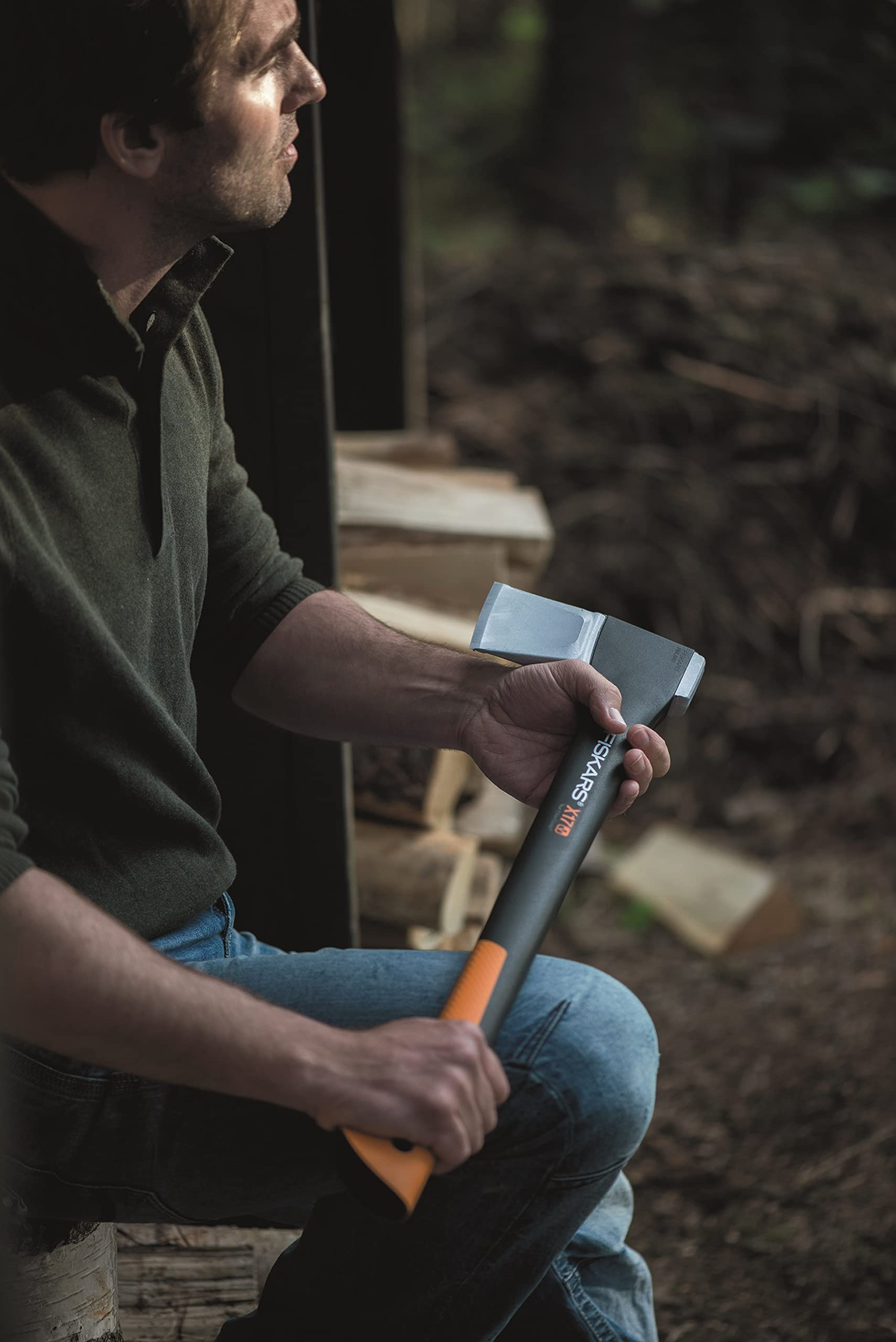Ein Mann sitzt im Wald auf einem Holzstamm und hält eine Fiskars Axt in den Händen.