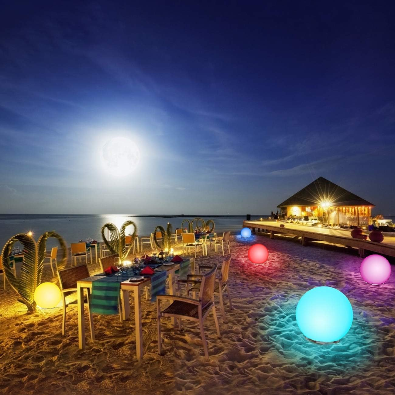 Ristorante sulla spiaggia illuminato di notte con tavoli, sfere luminose colorate nella sabbia e luna piena.