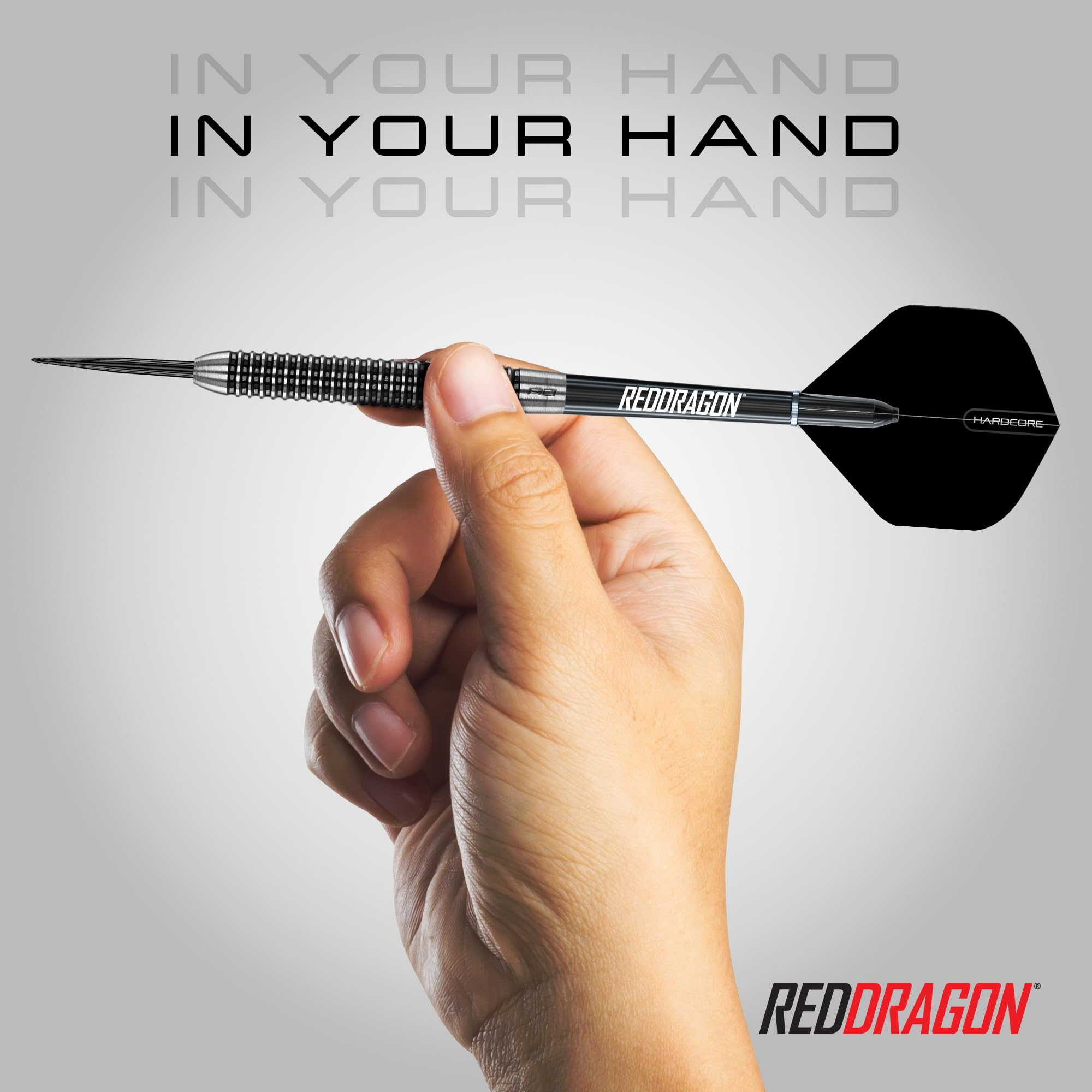 Eine Hand hält einen schwarzen Dartpfeil mit der Aufschrift „Red Dragon“ vor grauem Hintergrund.