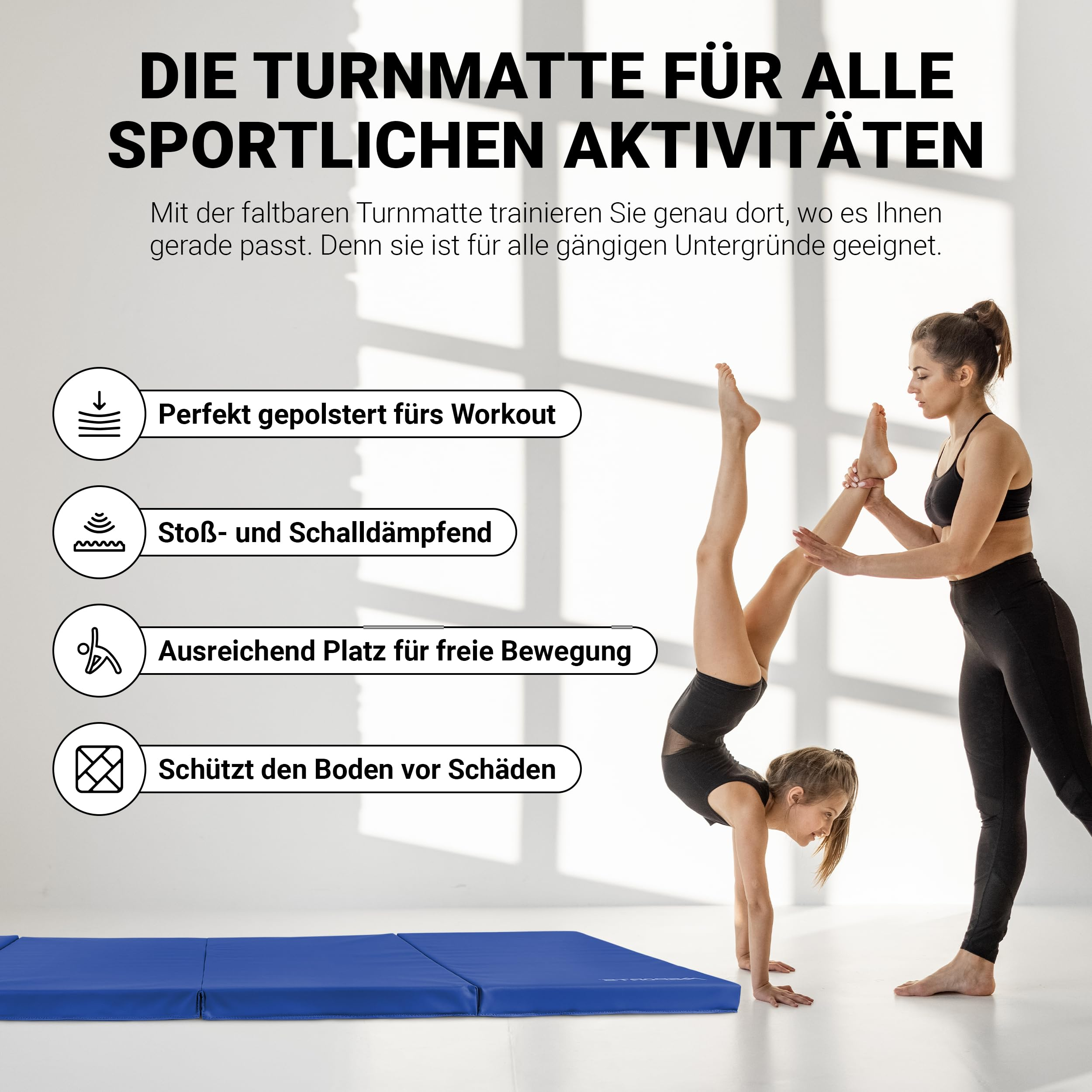 Eine Frau unterstützt ein Mädchen beim Handstand auf einer blauen Gymnastikmatte vor weißer Wand.