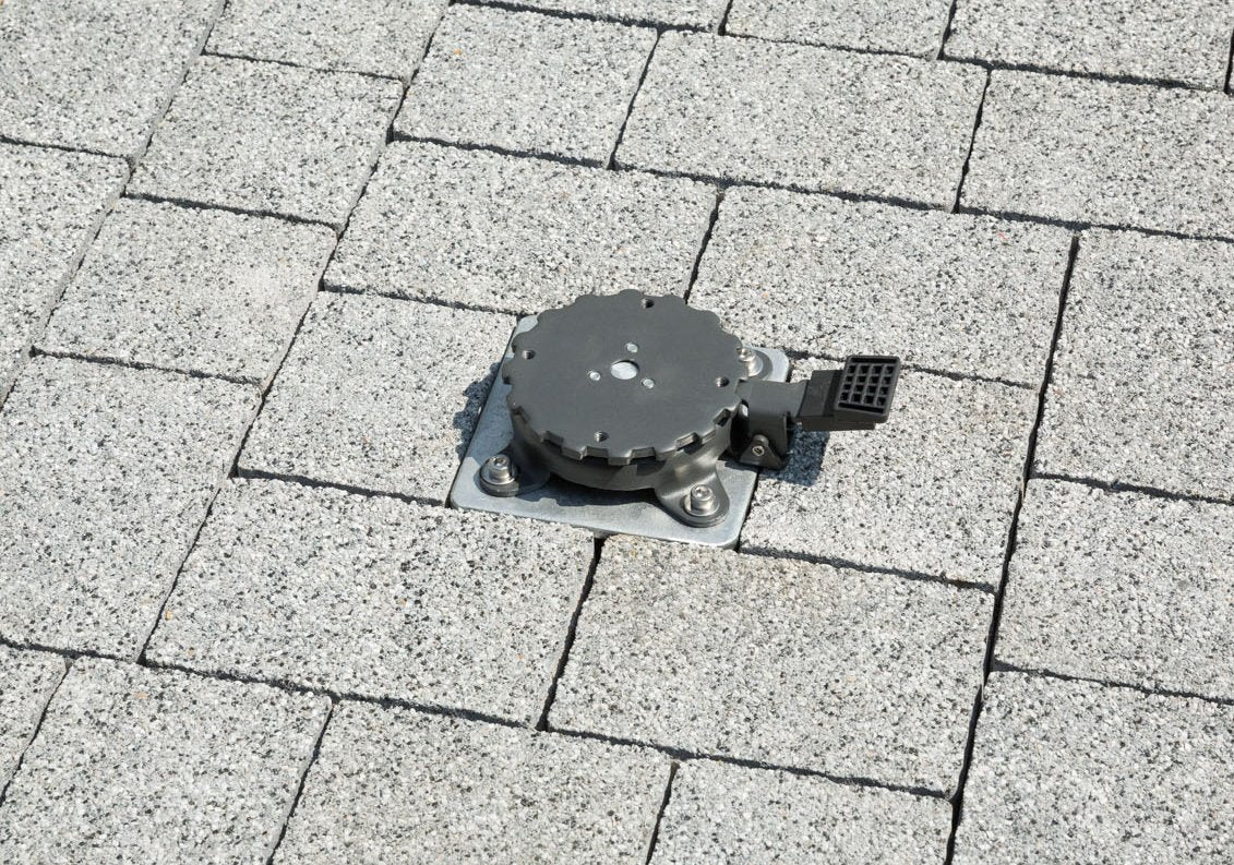 Ein schwarzes mechanisches Gerät in grauen Verbundsteinpflastern.