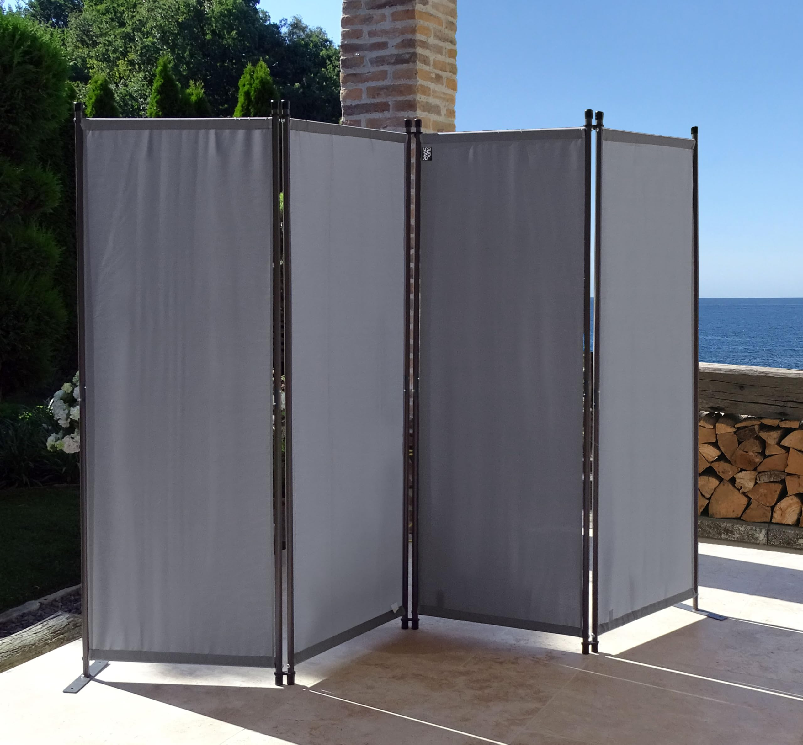 Ein grauer, vierteiliger Paravent auf einer sonnigen Terrasse mit Blick auf das Meer.