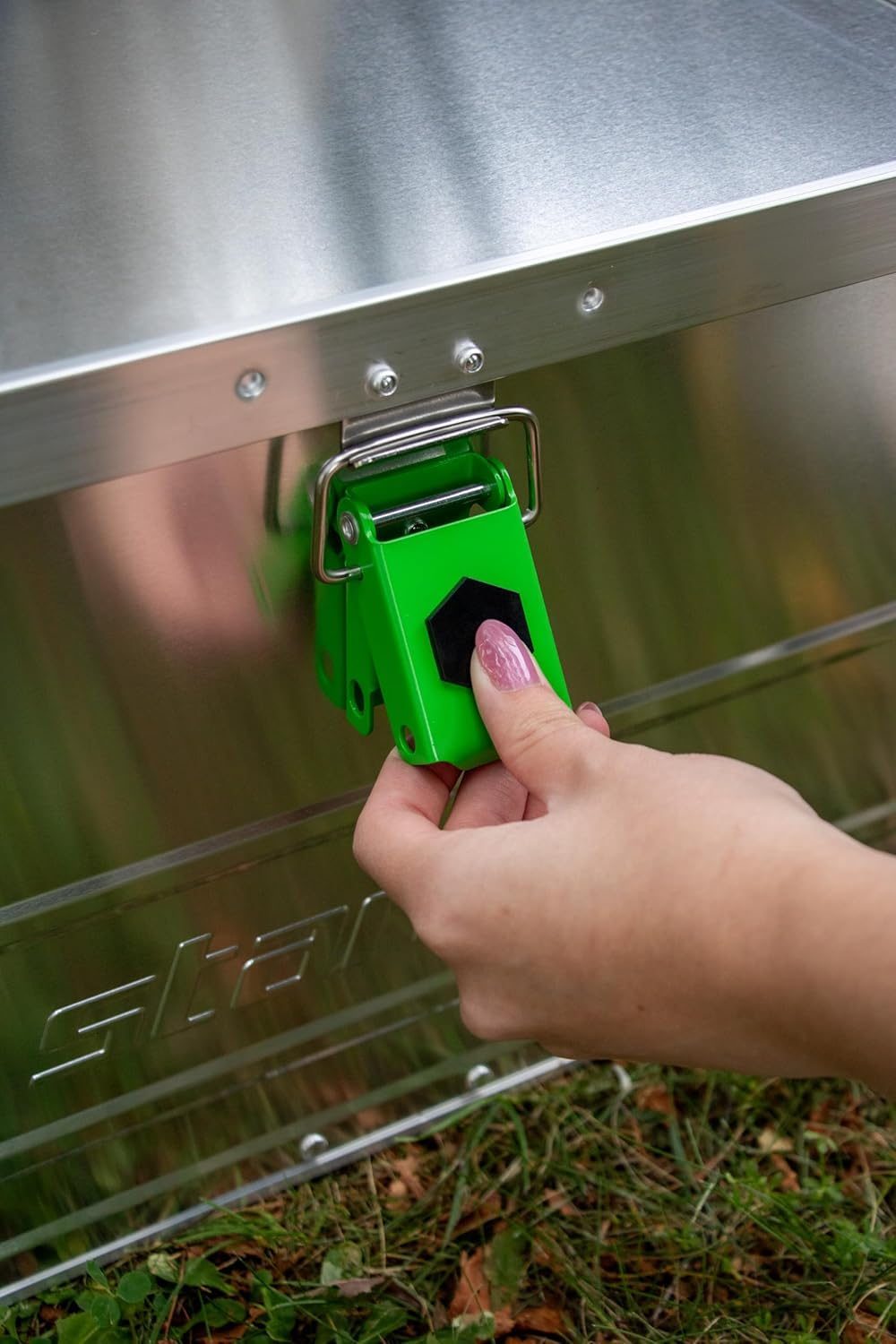 Una mano apre una chiusura verde su una scatola di metallo all'aperto.