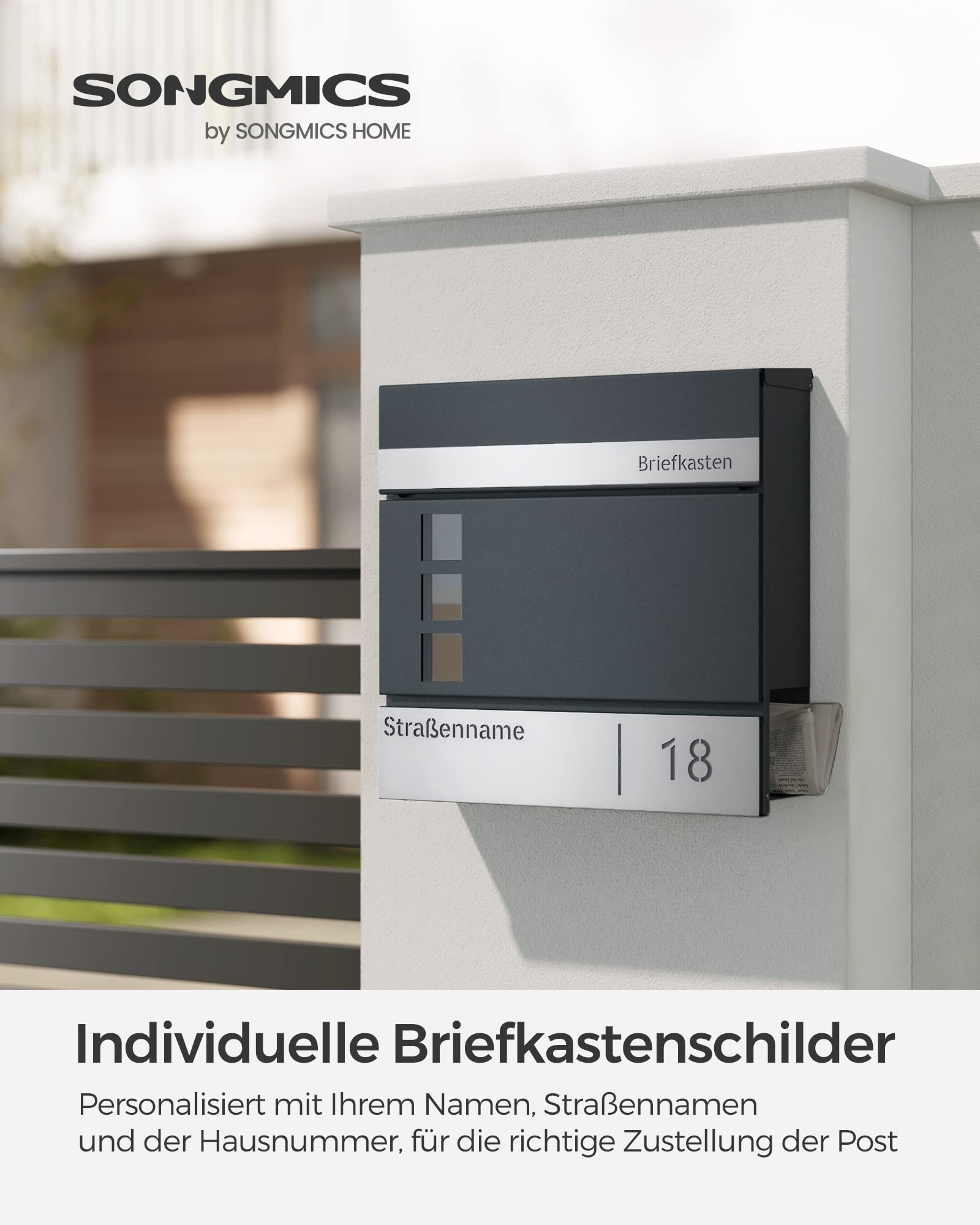 Une boîte aux lettres grise avec porte-journaux sur un mur clair, avec nom de rue et numéro.