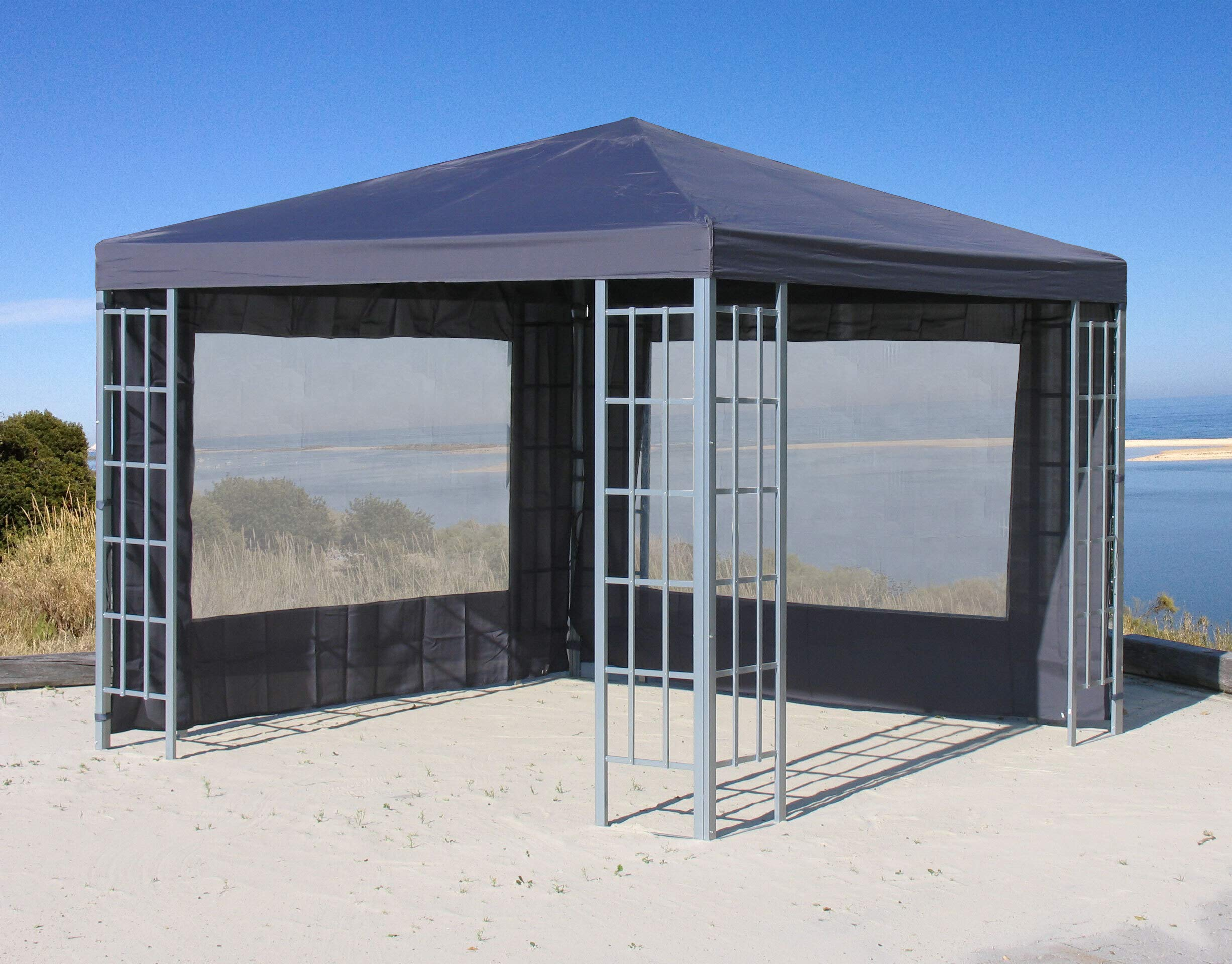Grauer Pavillon mit Fenstern und Metallrahmen am Strand unter blauem Himmel.