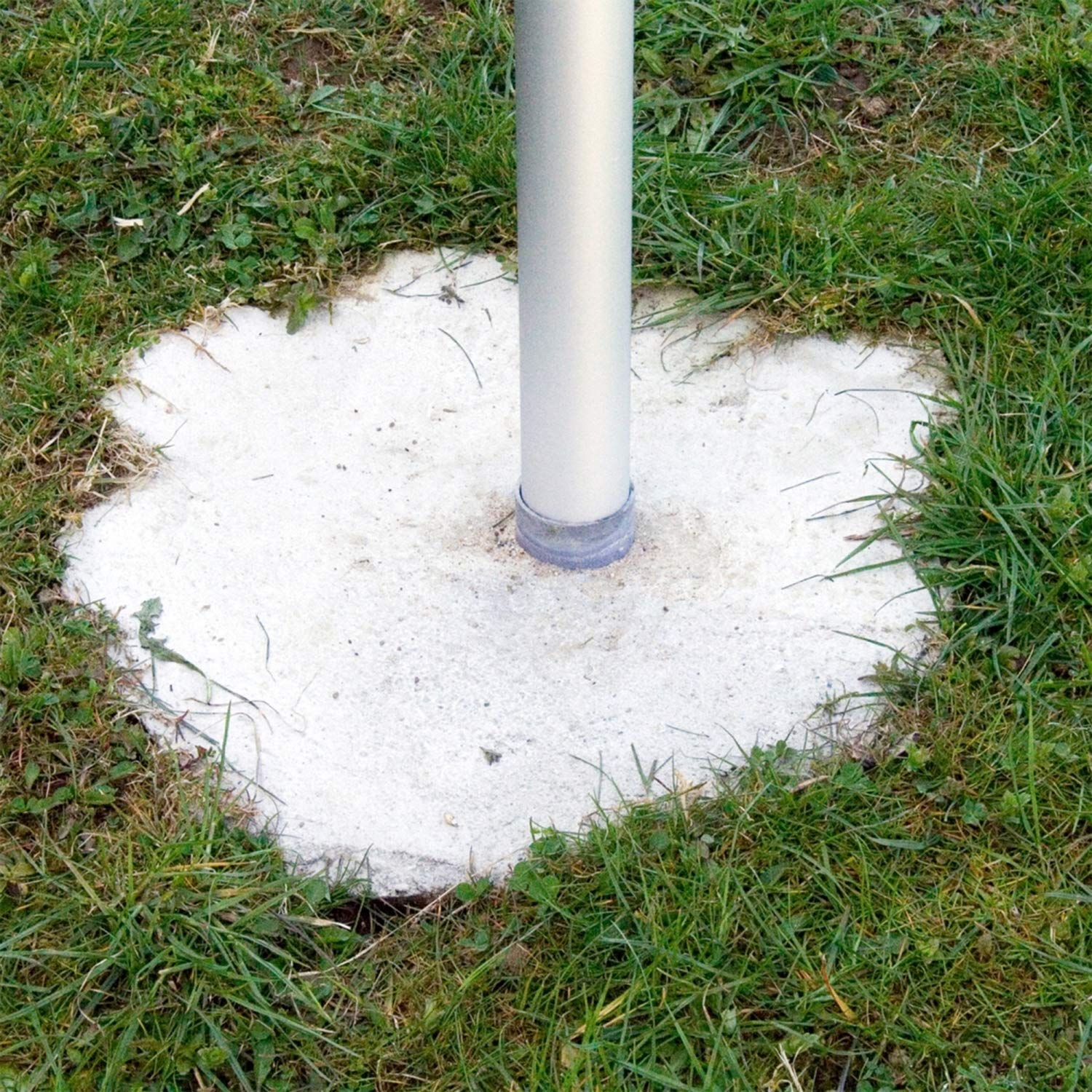 Un poteau en métal gris se dresse dans une fondation en béton de forme irrégulière dans l'herbe.