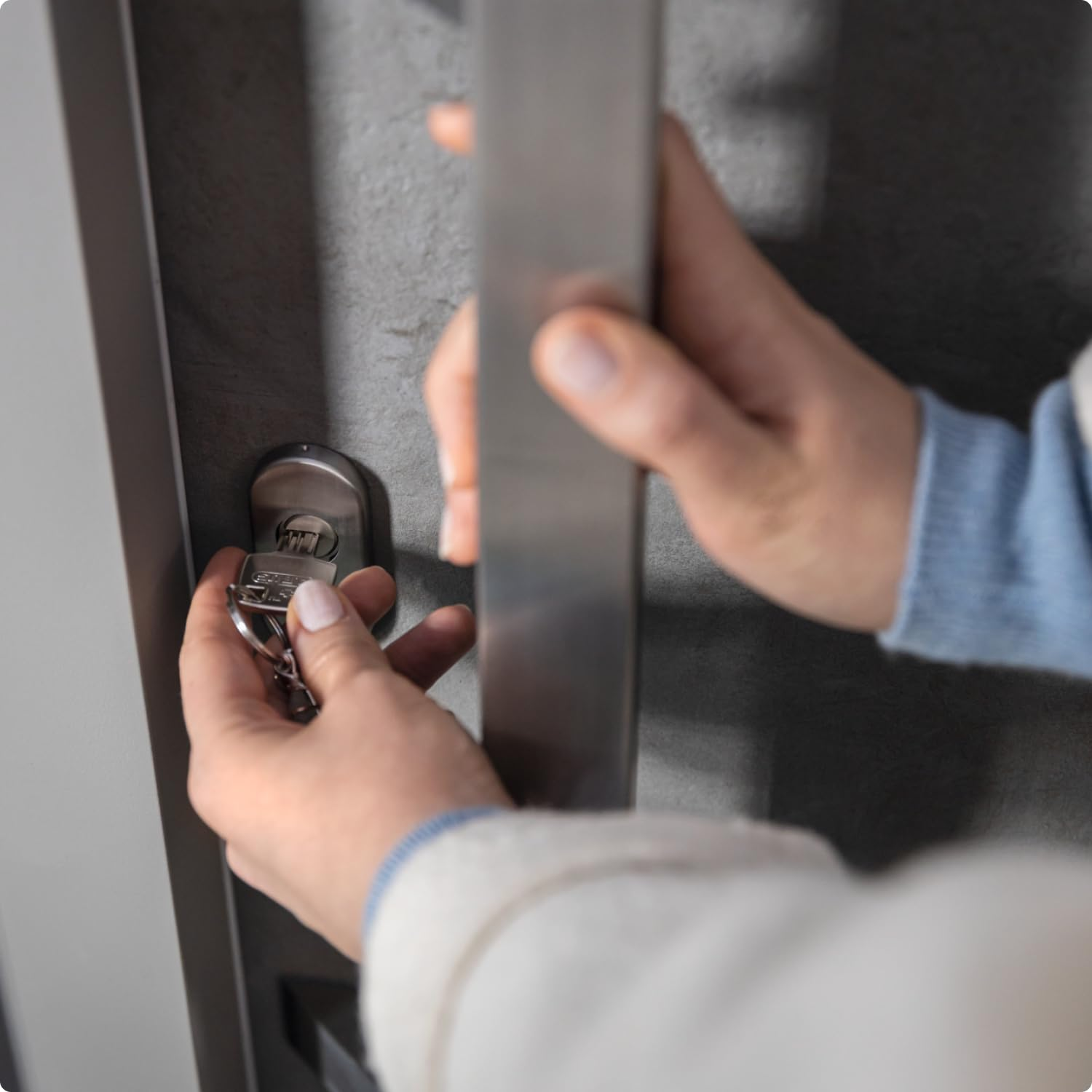 Eine Person schließt eine graue Tür mit einem Schlüssel auf und hält den Metallgriff.