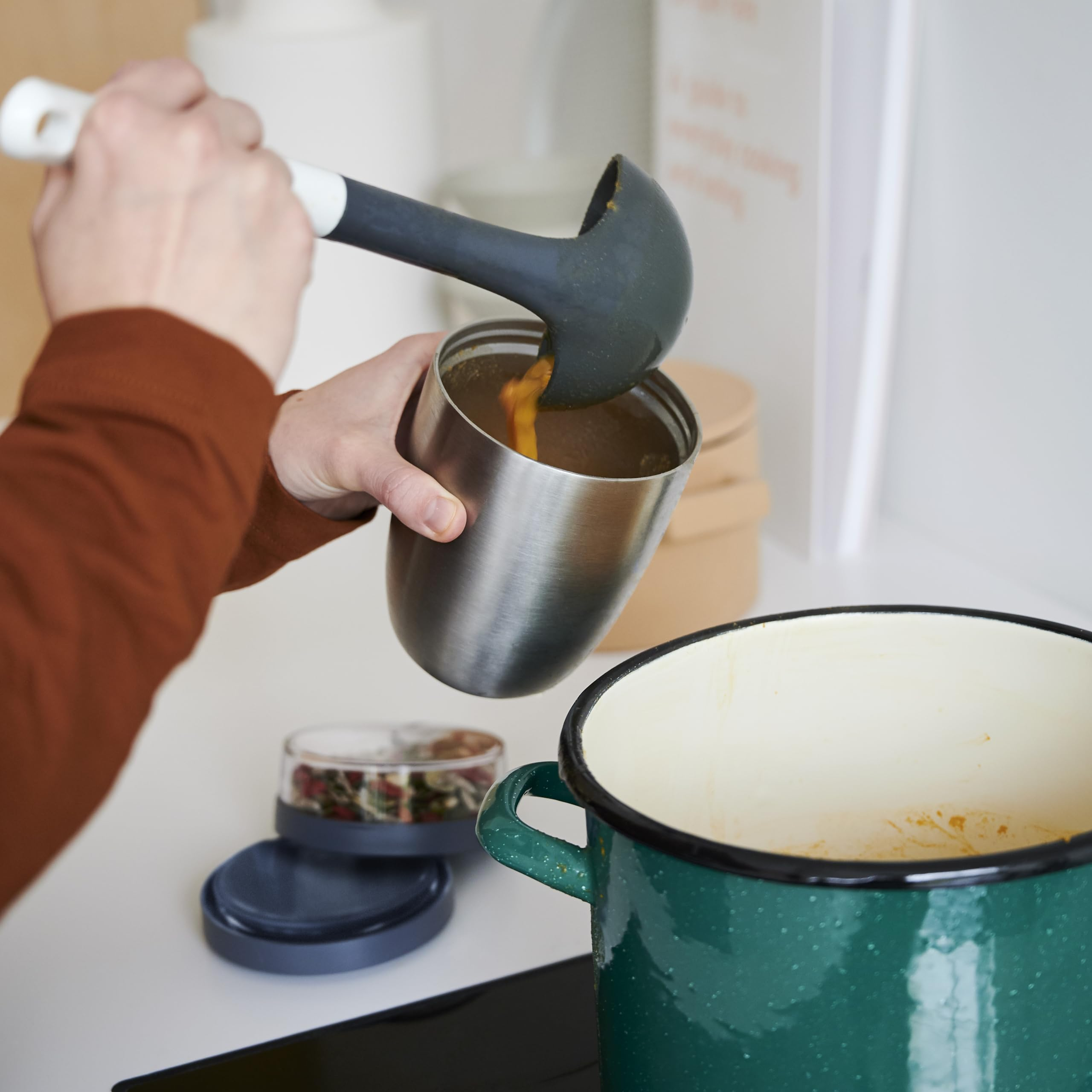 Una persona usa un mestolo per versare la zuppa da una pentola verde in una tazza.