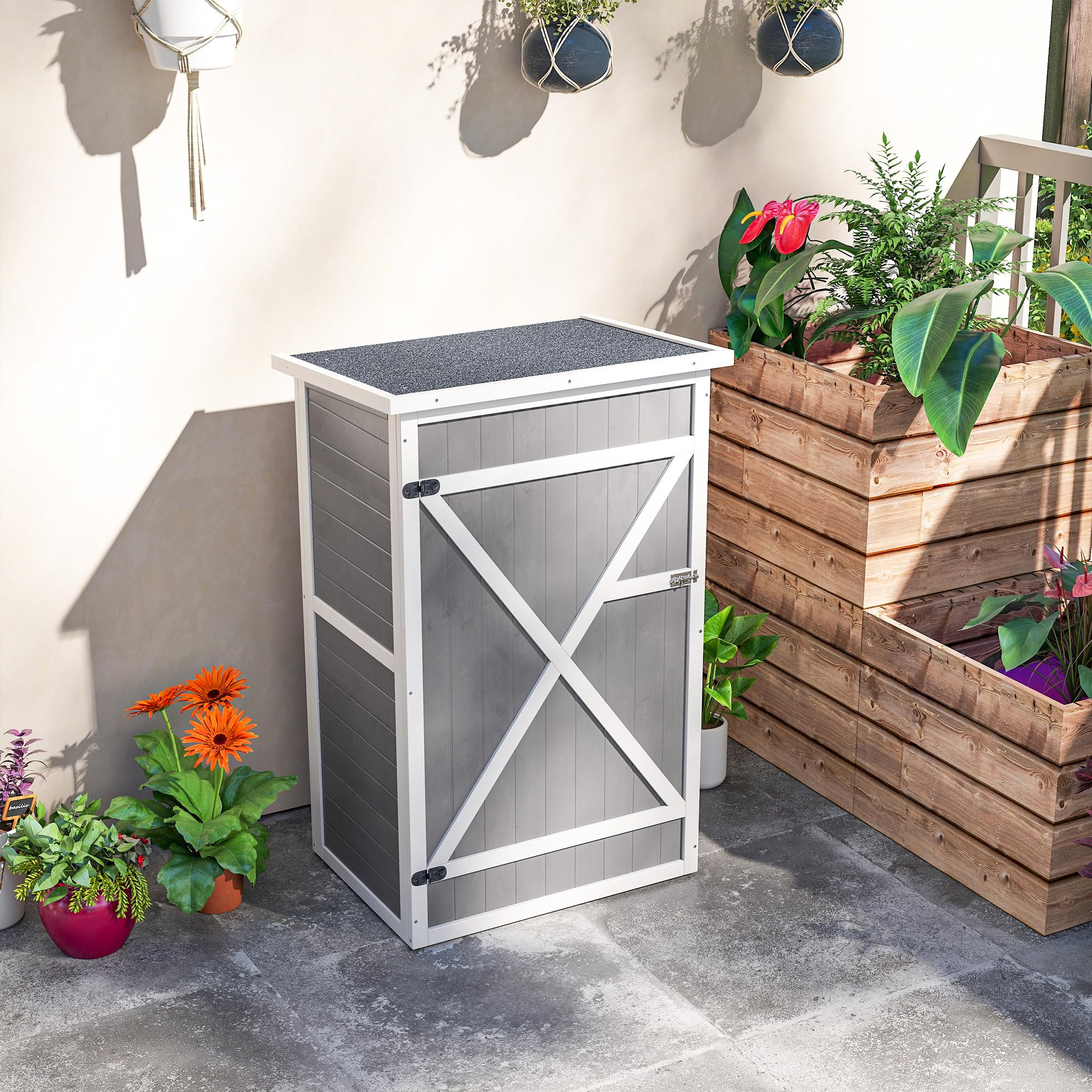 Ein grauer und weißer Gartenschrank aus Holz mit dunklem Dach auf einer Terrasse mit Topfpflanzen.