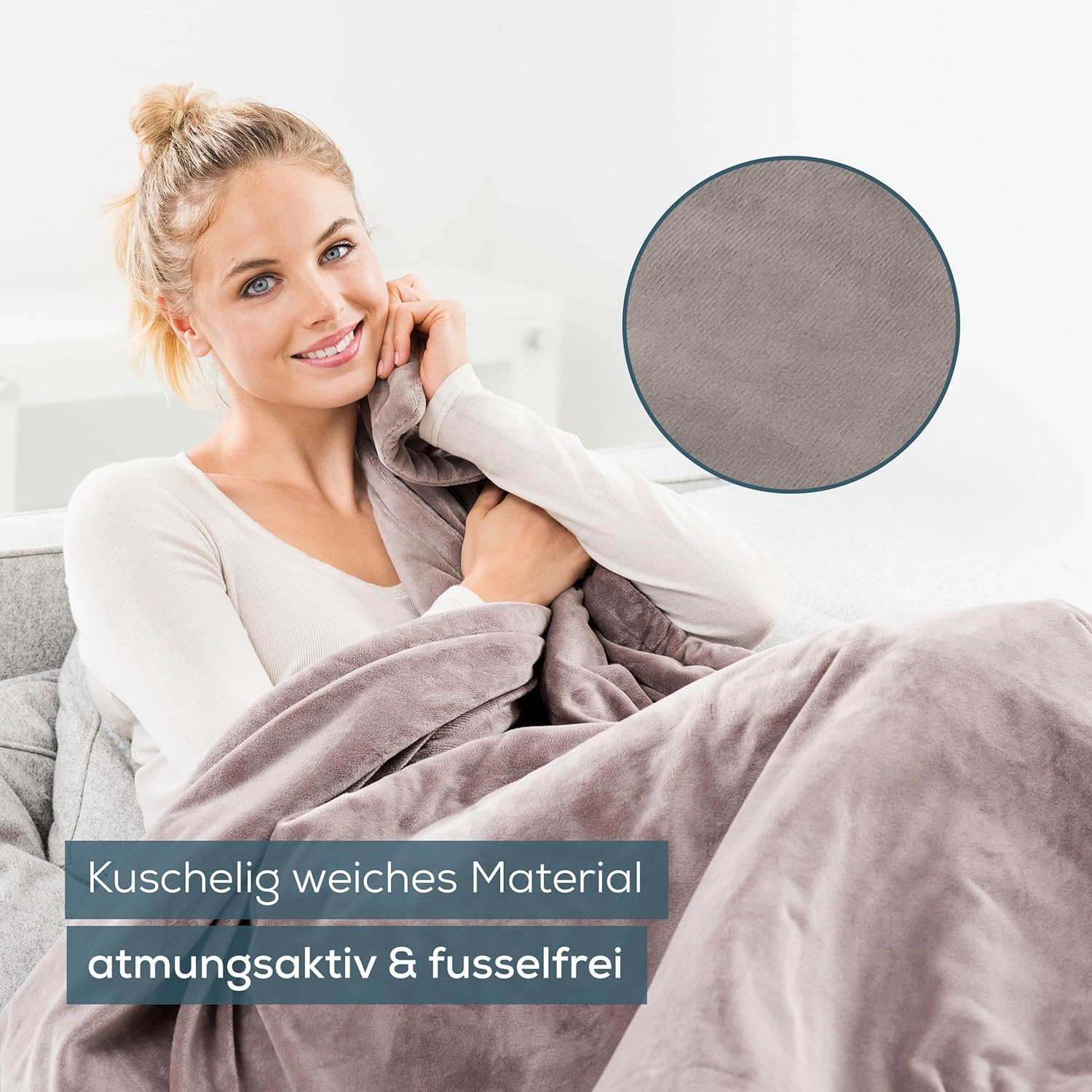 Una donna sorridente è seduta su un divano, avvolta in una morbida coperta grigia.
