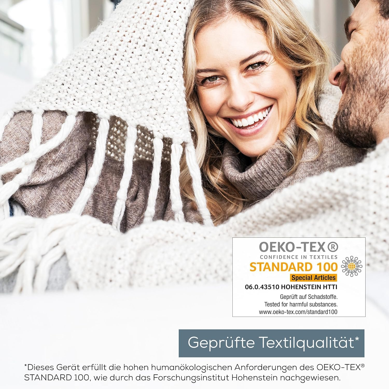 Coppia sorridente avvolta in coperta bianca, con logo e testo OEKO-TEX.
