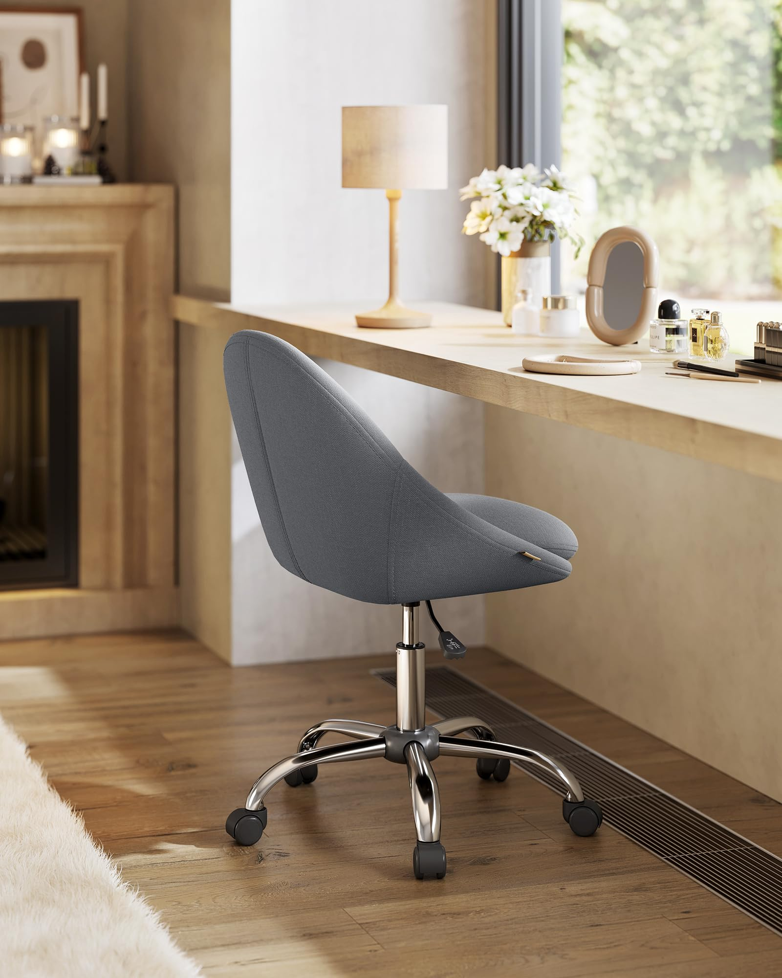 Une chaise de bureau grise à roulettes devant un bureau en bois avec lampe et miroir.