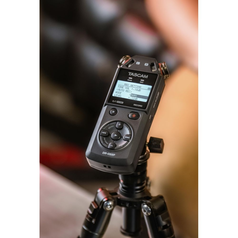 Un enregistreur audio Tascam DR-05XP noir fixé sur un petit trépied sur un fond flou.