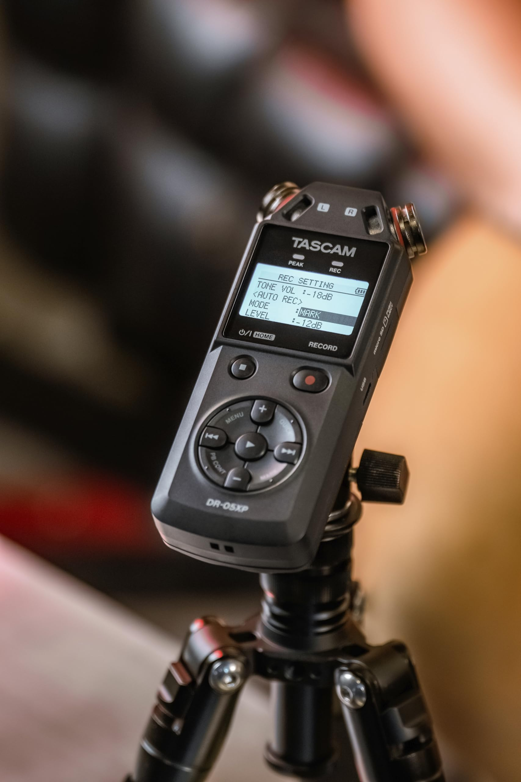 Un enregistreur audio Tascam DR-05XP noir sur trépied avec écran allumé.