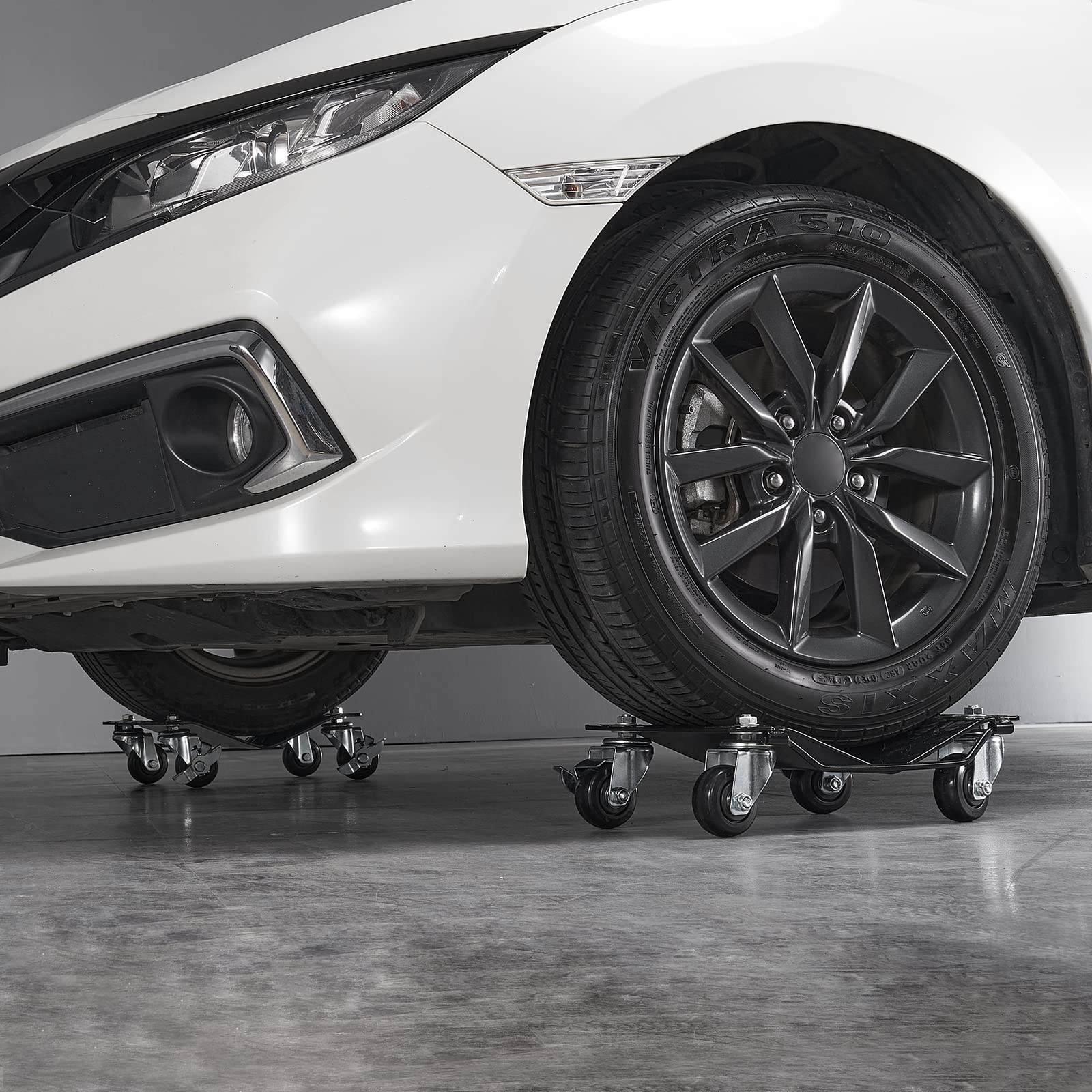 Ein weißes Auto steht auf vier kleinen Rollbrettern in einer Garage mit Betonboden.