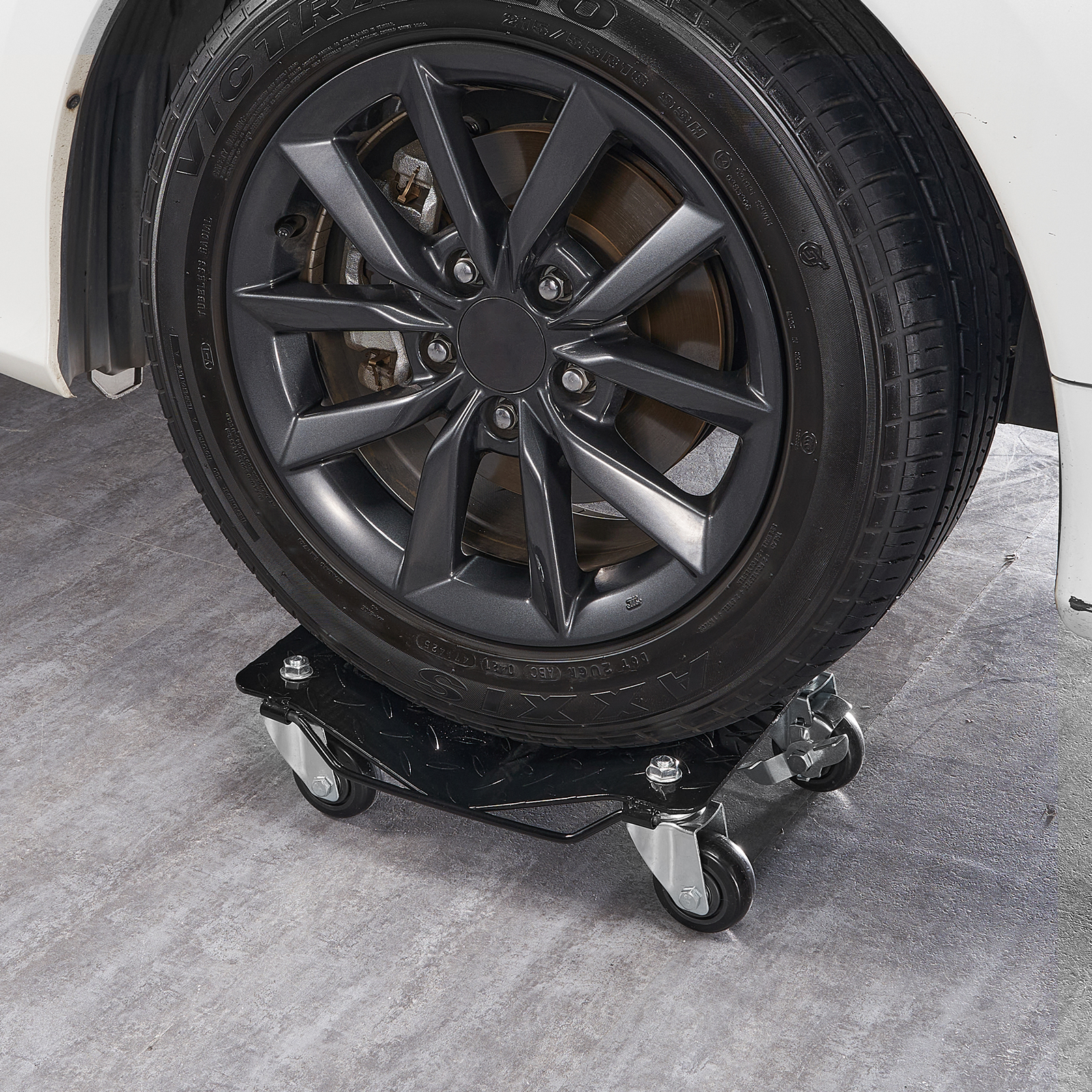 Ein Autoreifen auf einer schwarzen Werkstattrolle mit vier Rollen auf einem grauen Boden.