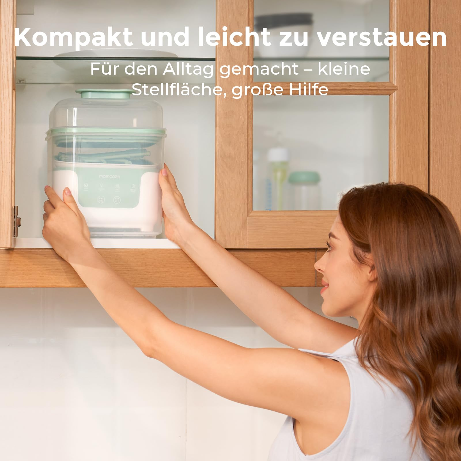 Une femme place un appareil blanc et vert dans un meuble de cuisine en bois.