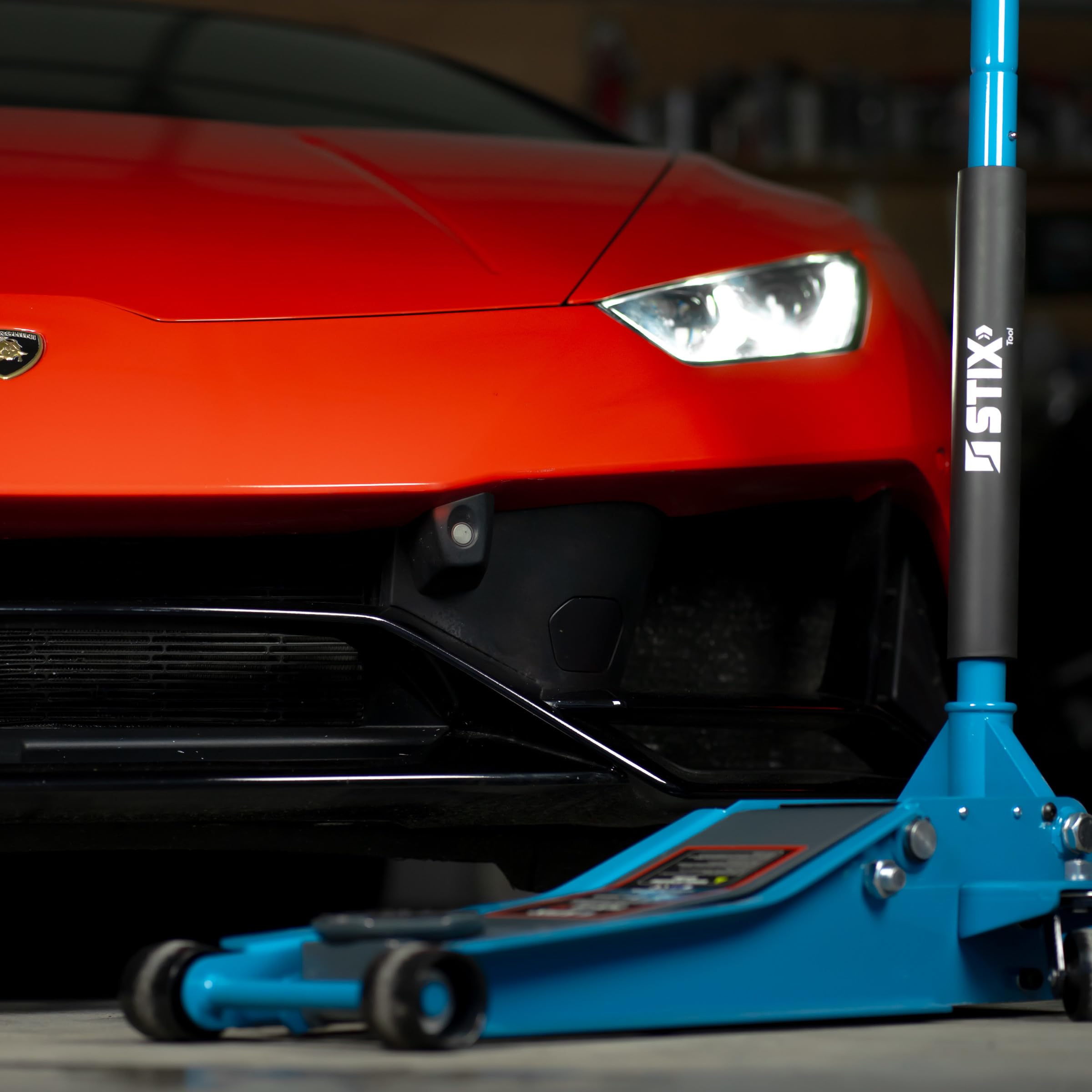 Un cric idraulico blu Stix si trova davanti a un'auto sportiva rossa in un garage.
