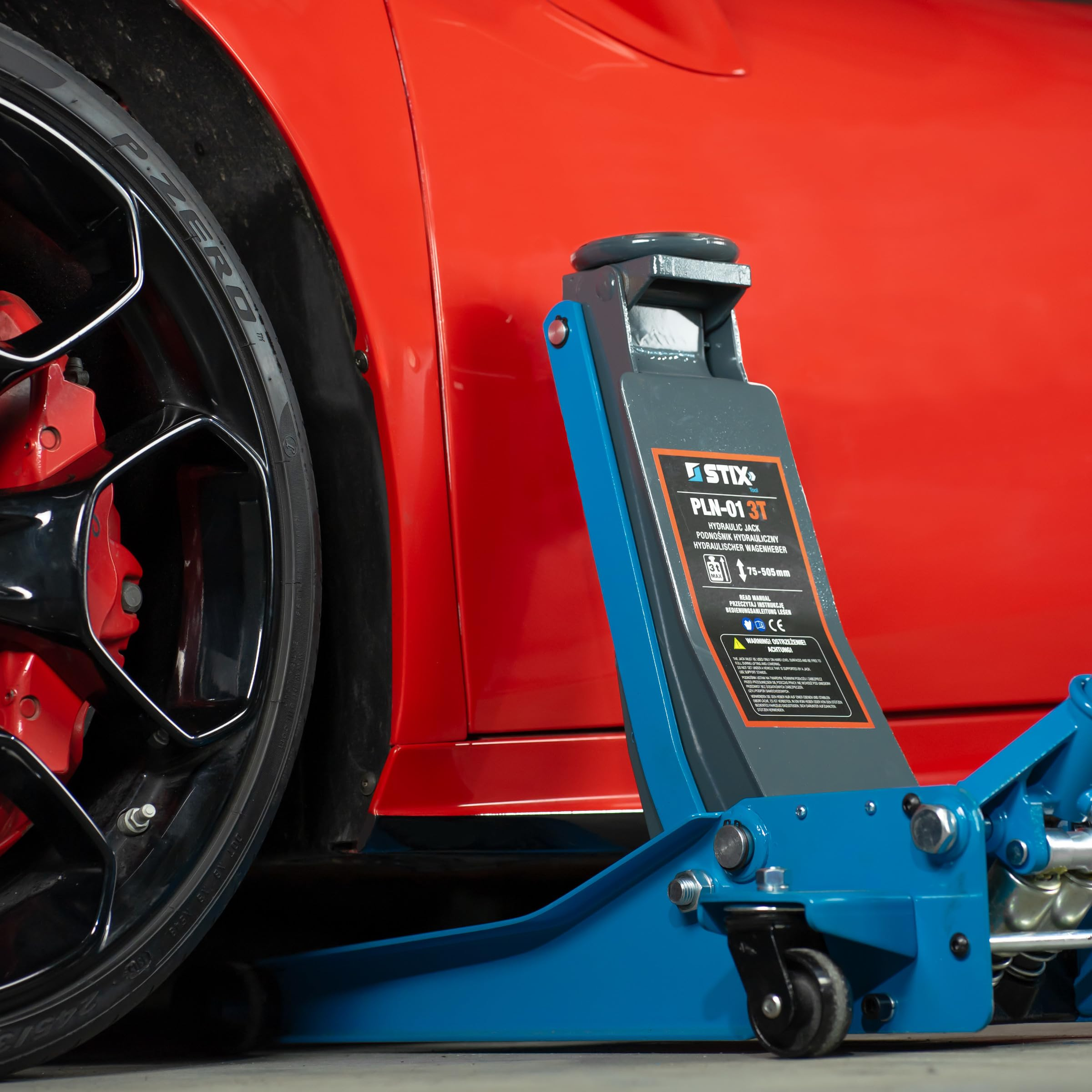 Un cric idraulico blu per auto si trova accanto all'auto rossa.