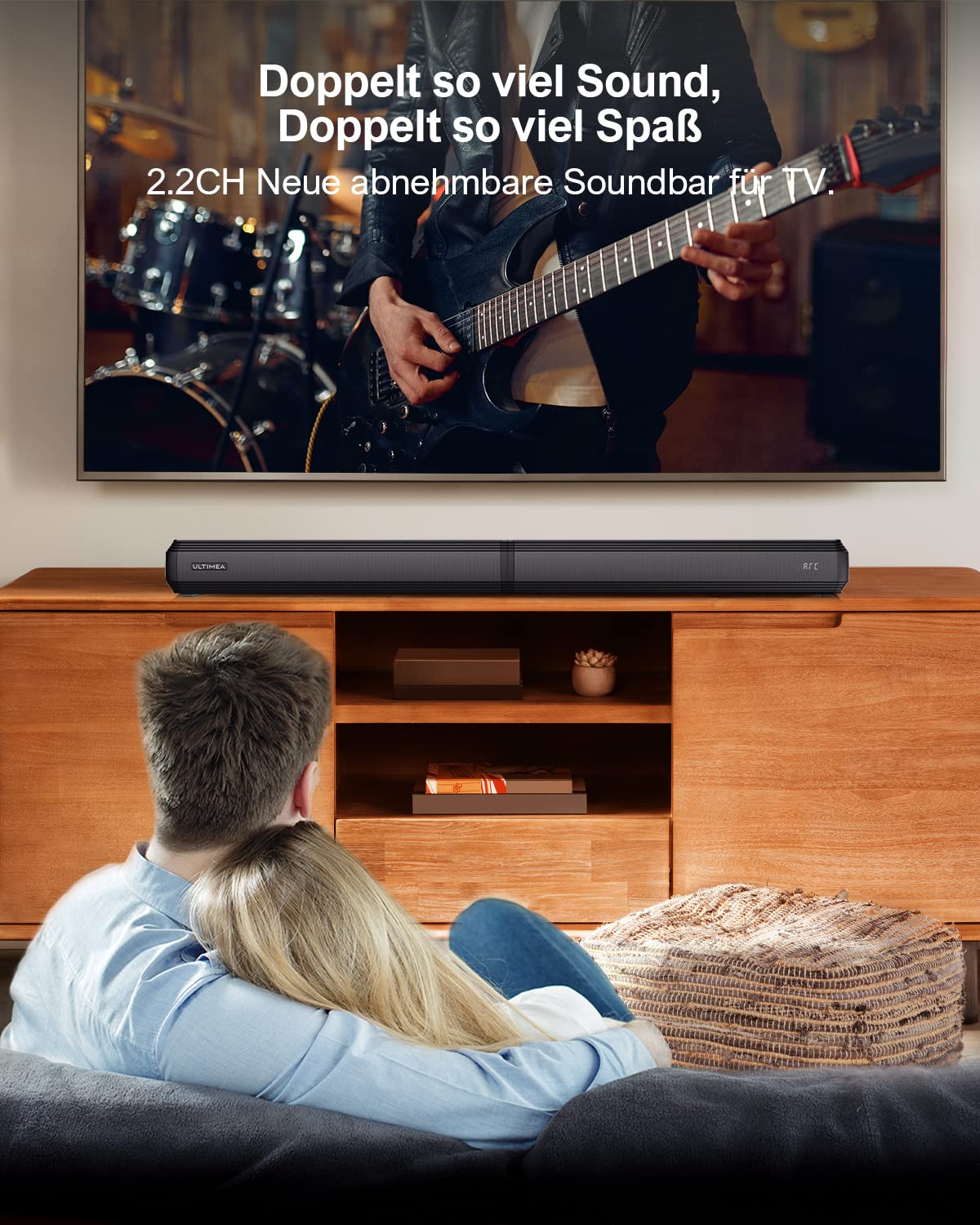 Un couple est assis sur le canapé devant une télé avec barre de son, regardant un concert.