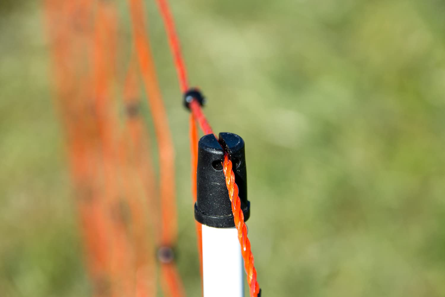 Un poteau blanc avec un sommet noir soutient une clôture électrique orange sur un fond vert flou.