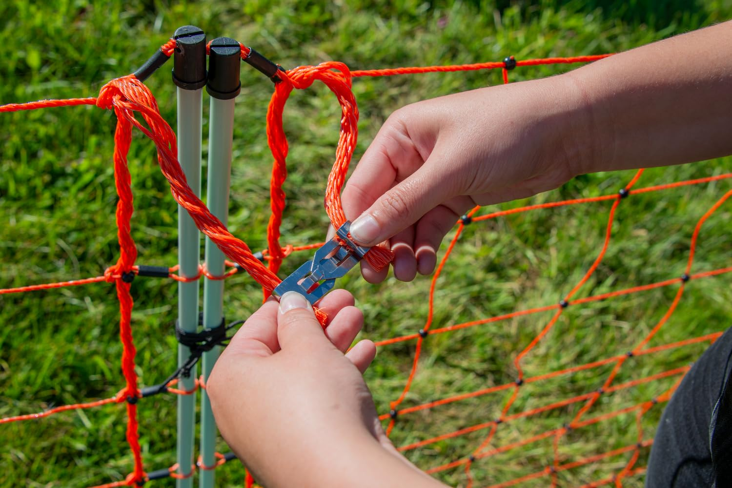 Des mains connectent un filet de clôture électrique orange à un piquet blanc.
