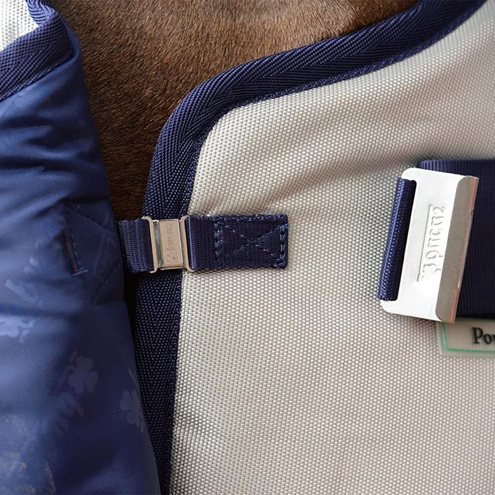 Gros plan d'une couverture de cheval bleue et beige avec des boucles argentées et un logo.