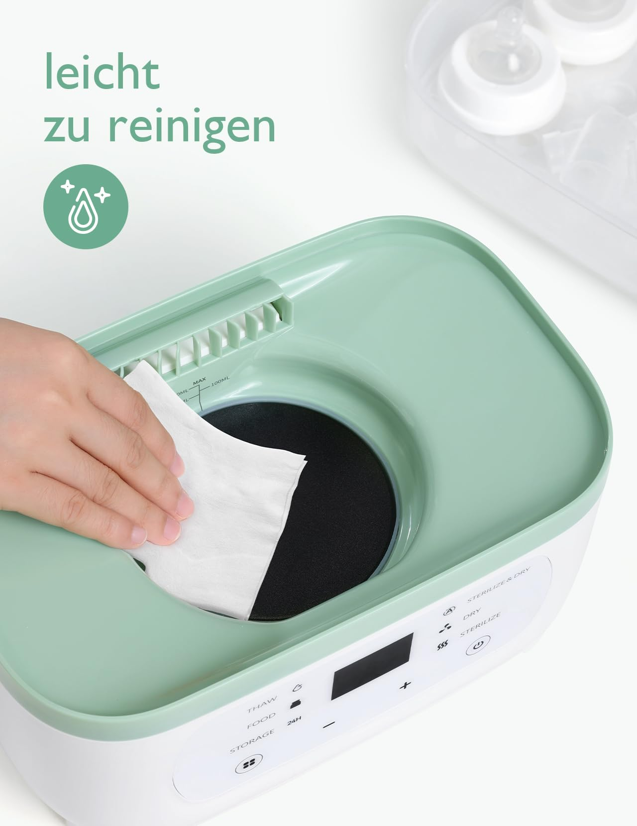 Une main essuie l'intérieur d'un chauffe-biberon vert et blanc avec un chiffon.