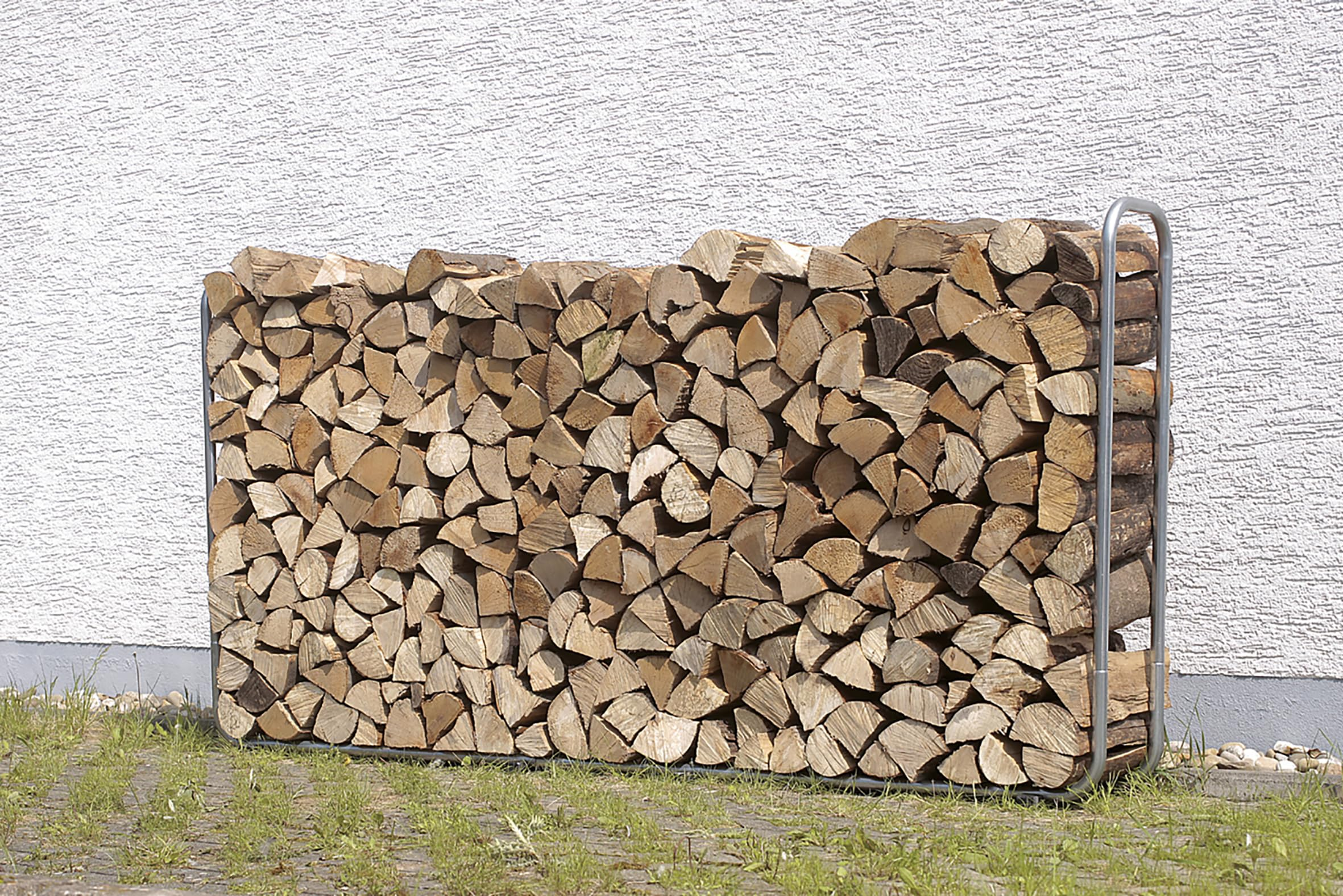 Une pile bien rangée de bois de chauffage fendu est stockée dans un support métallique contre un mur blanc.