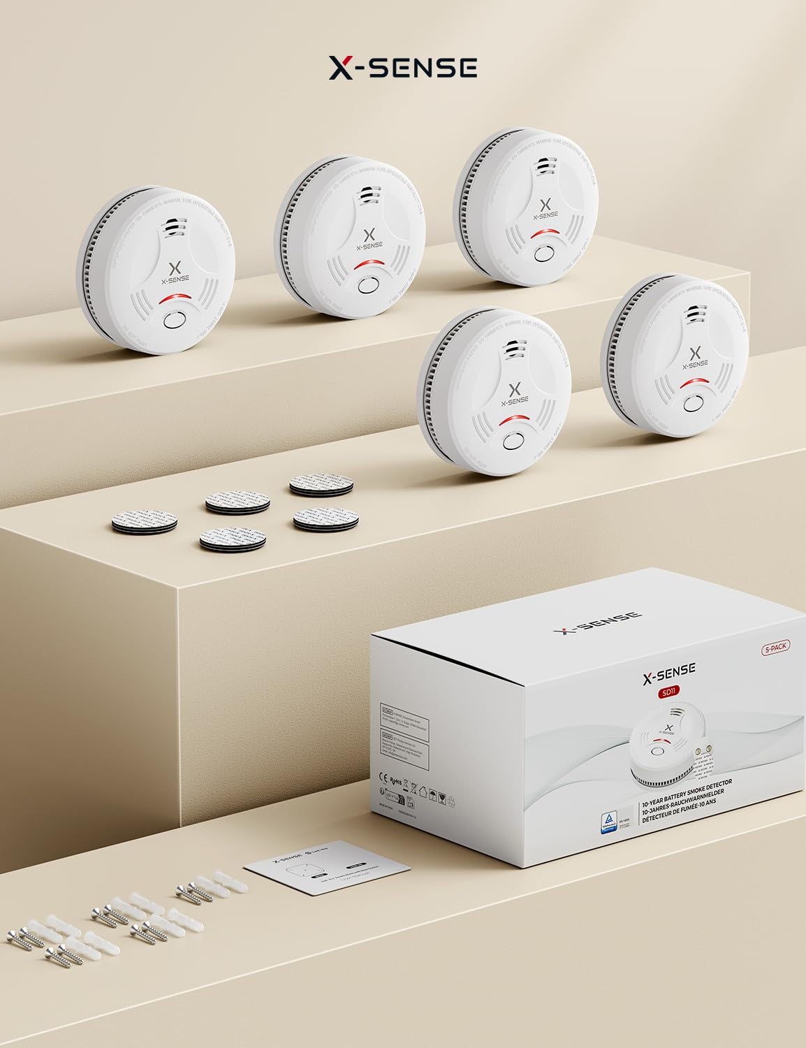 Cinq détecteurs de fumée blancs X-Sense avec patins de fixation, vis et boîte de produit sur fond beige.
