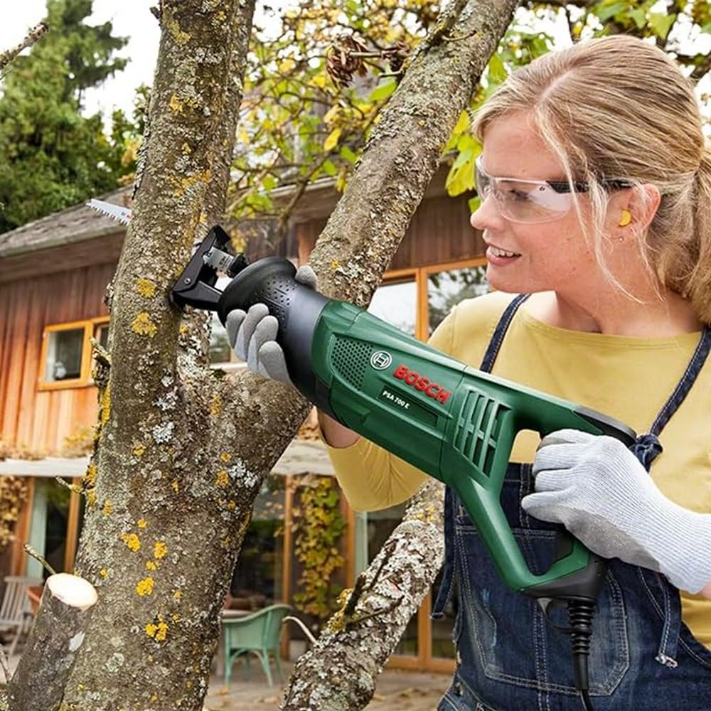 Una donna con occhiali protettivi e guanti taglia il ramo di un albero con un seghetto verde Bosch.