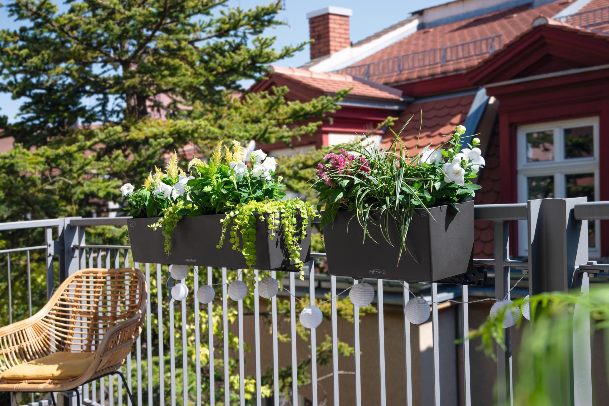Balcon avec jardinières, guirlande lumineuse et chaise en osier devant une vieille façade.