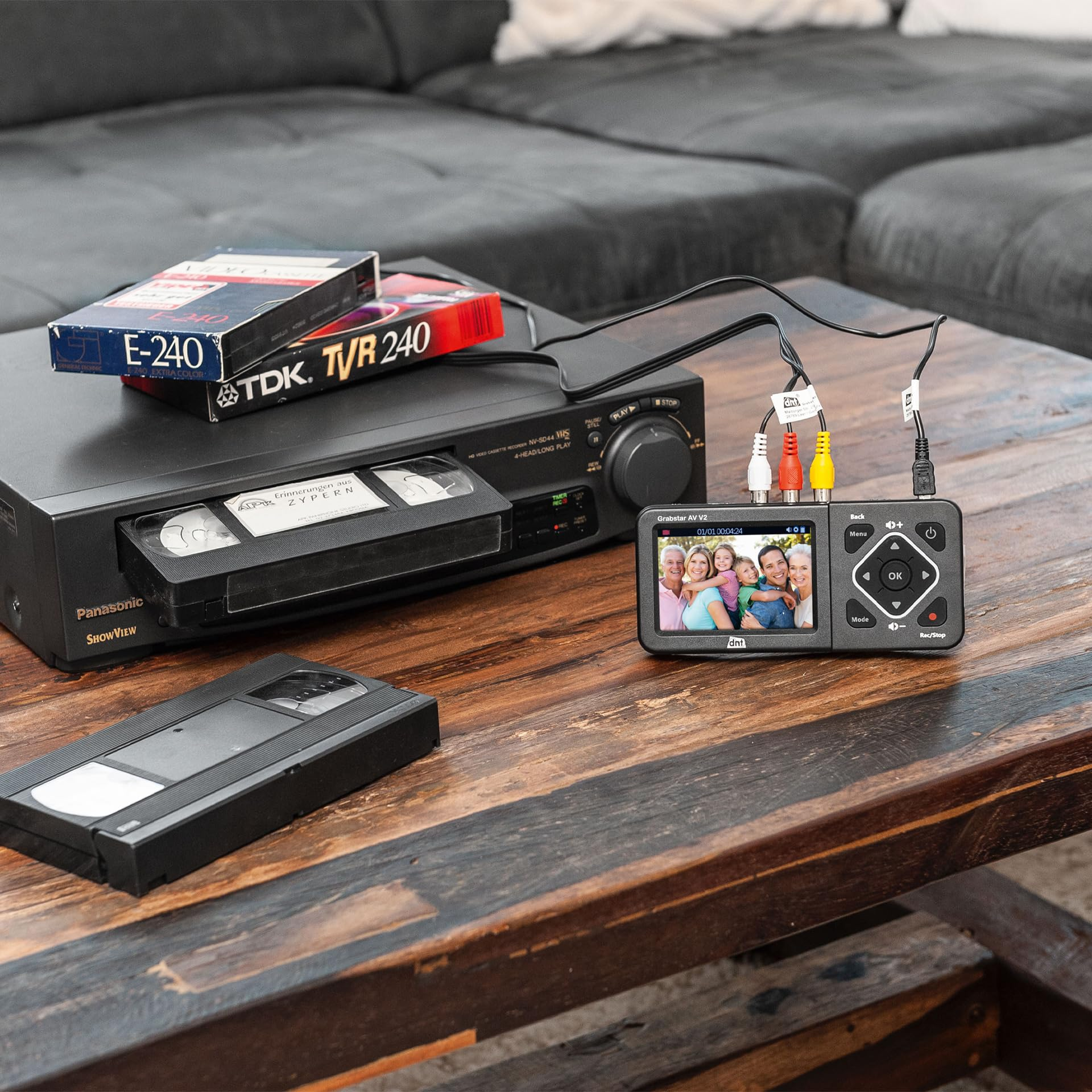 Un magnétoscope, des cassettes VHS et un petit appareil de capture avec écran sur une table en bois.
