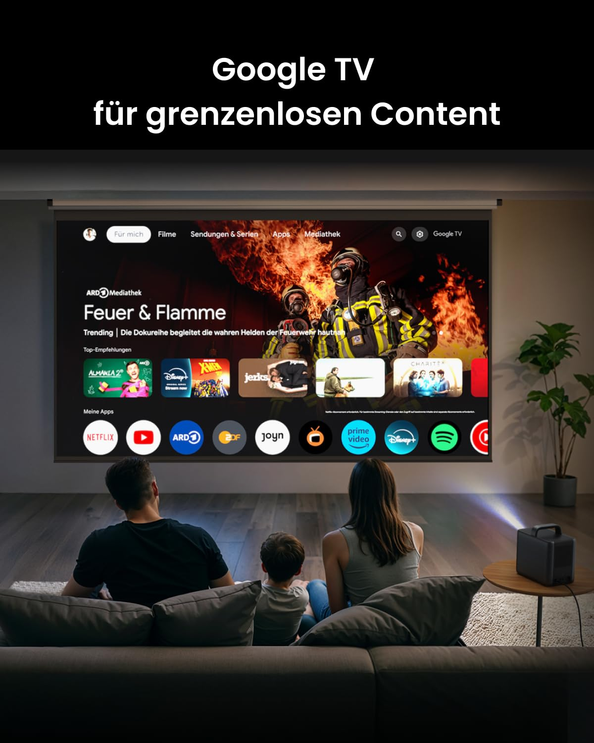 Eine Familie sitzt auf einem Sofa und schaut einen Film auf einer großen Leinwand, die von einem kleinen Projektor beleuchtet wird.