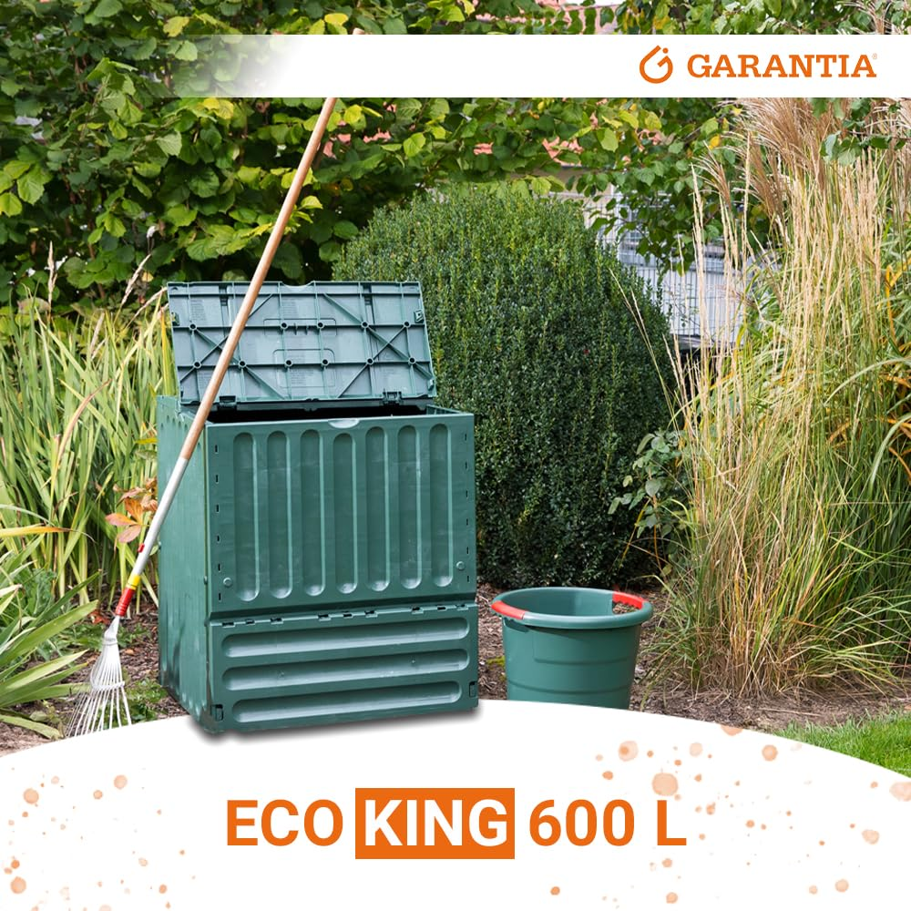 Composteur vert ECO KING 600 L dans un jardin avec un râteau et un seau près des buissons.