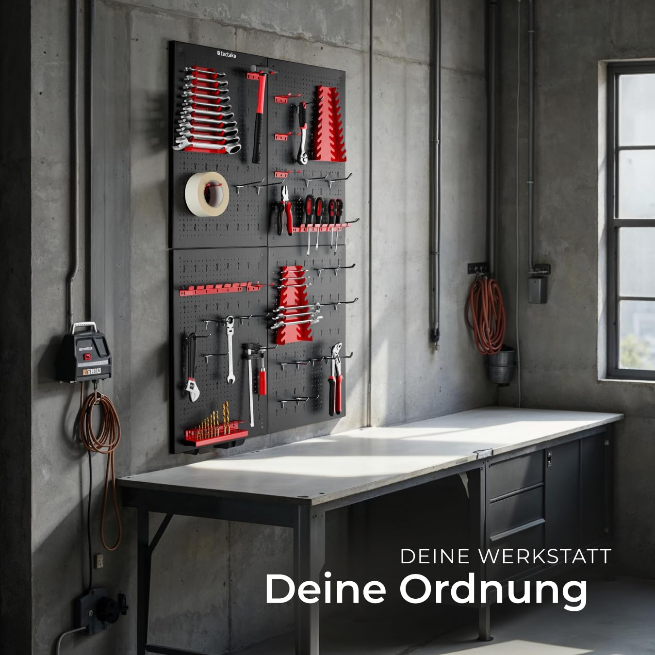 Ein schwarzer Werkzeughalter mit roten und silbernen Werkzeugen hängt über einer Werkbank an einer Betonwand.