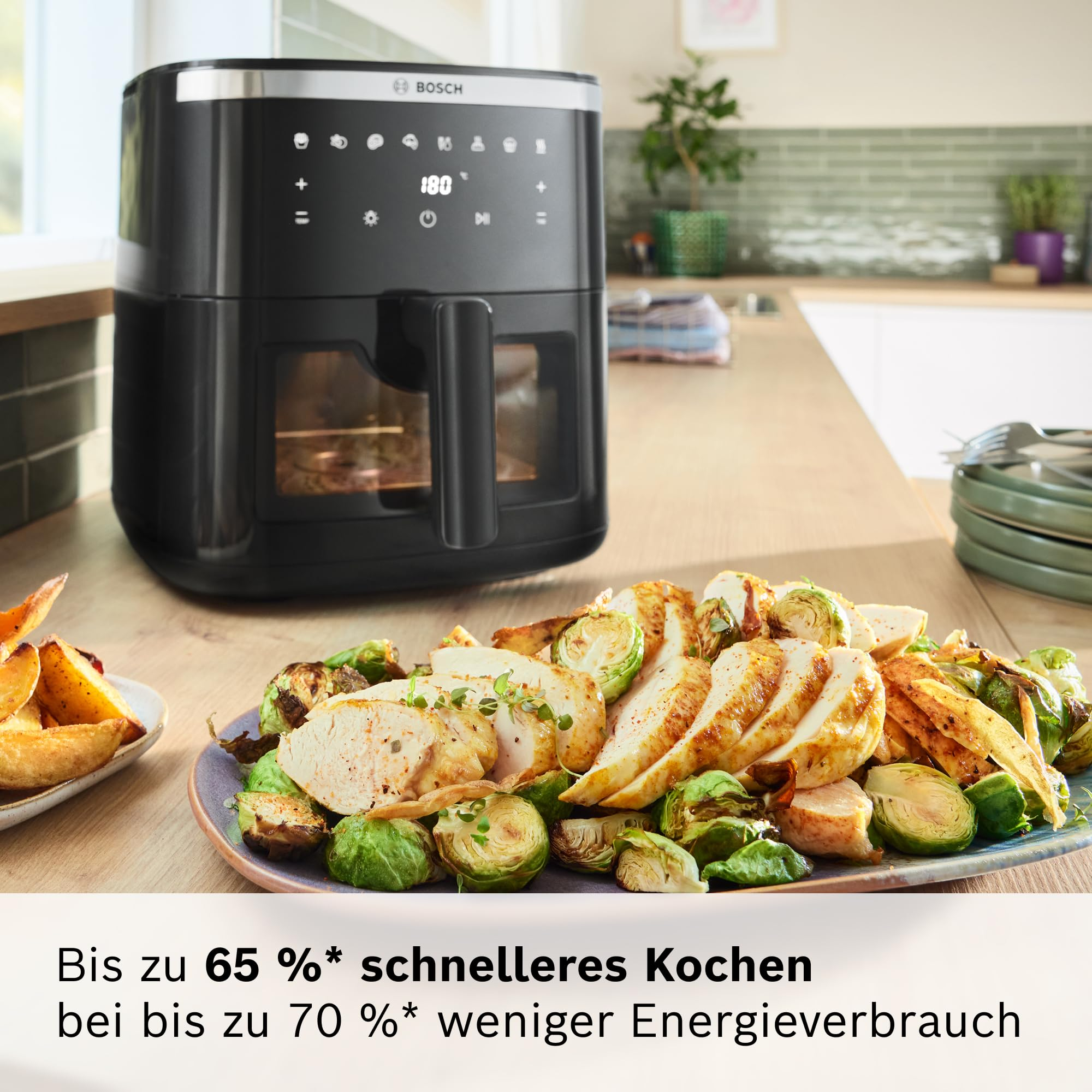 Friteuse à air Bosch noire sur un comptoir de cuisine à côté d'une assiette de poulet tranché et de choux de Bruxelles.